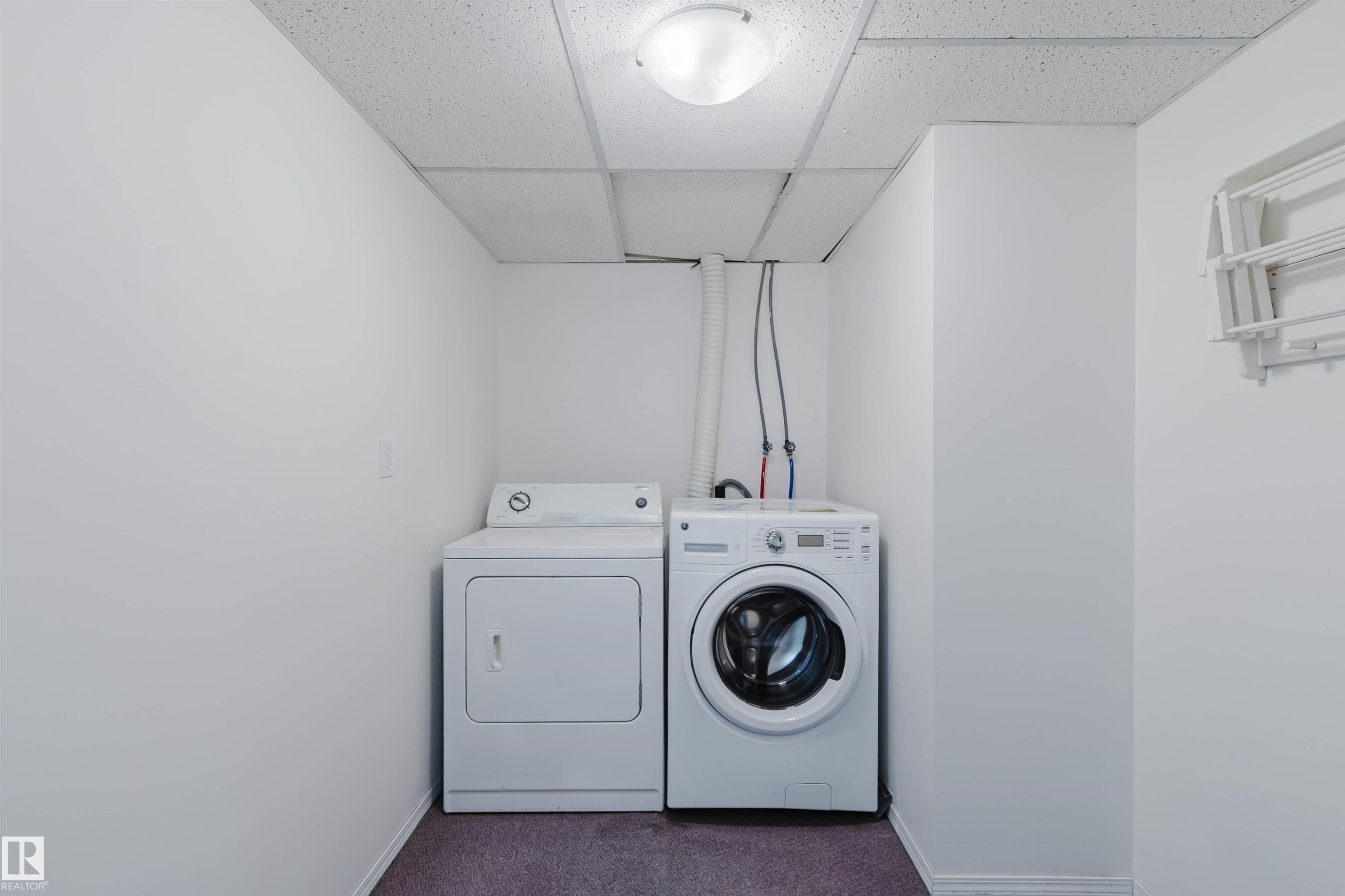 Dedicated laundry area featuring a front-load washing machine, a white dryer, and a neutral wall-mounted drying rack - 13755 131B Avenue, Edmonton, AB - Indoor Photo Showing Laundry Room