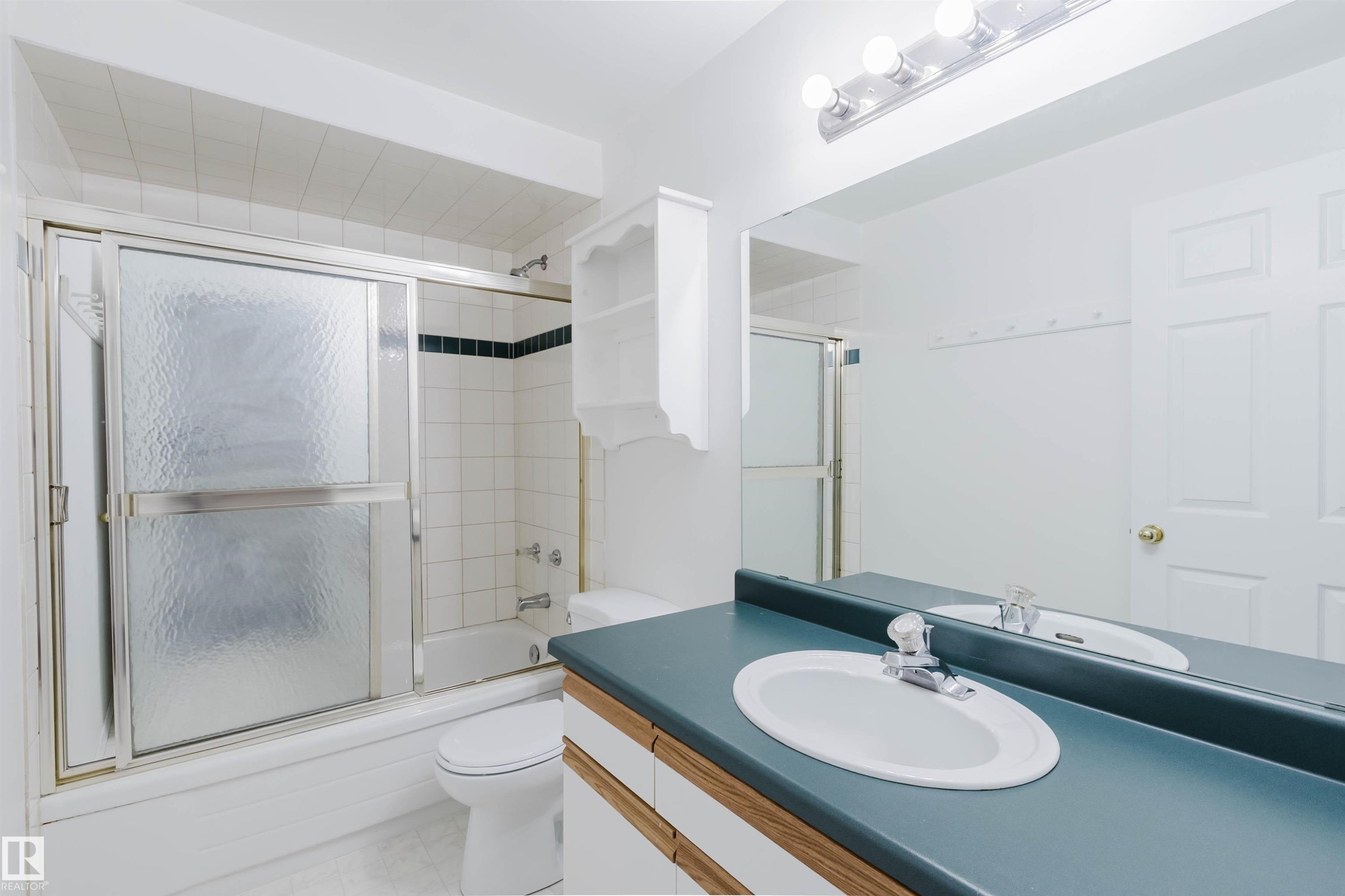 Bathroom featuring a full-width mirror, light wood-finish vanity with dual sinks, and a tub/shower combination with sliding frosted glass doors - 13755 131B Avenue, Edmonton, AB - Indoor Photo Showing Bathroom
