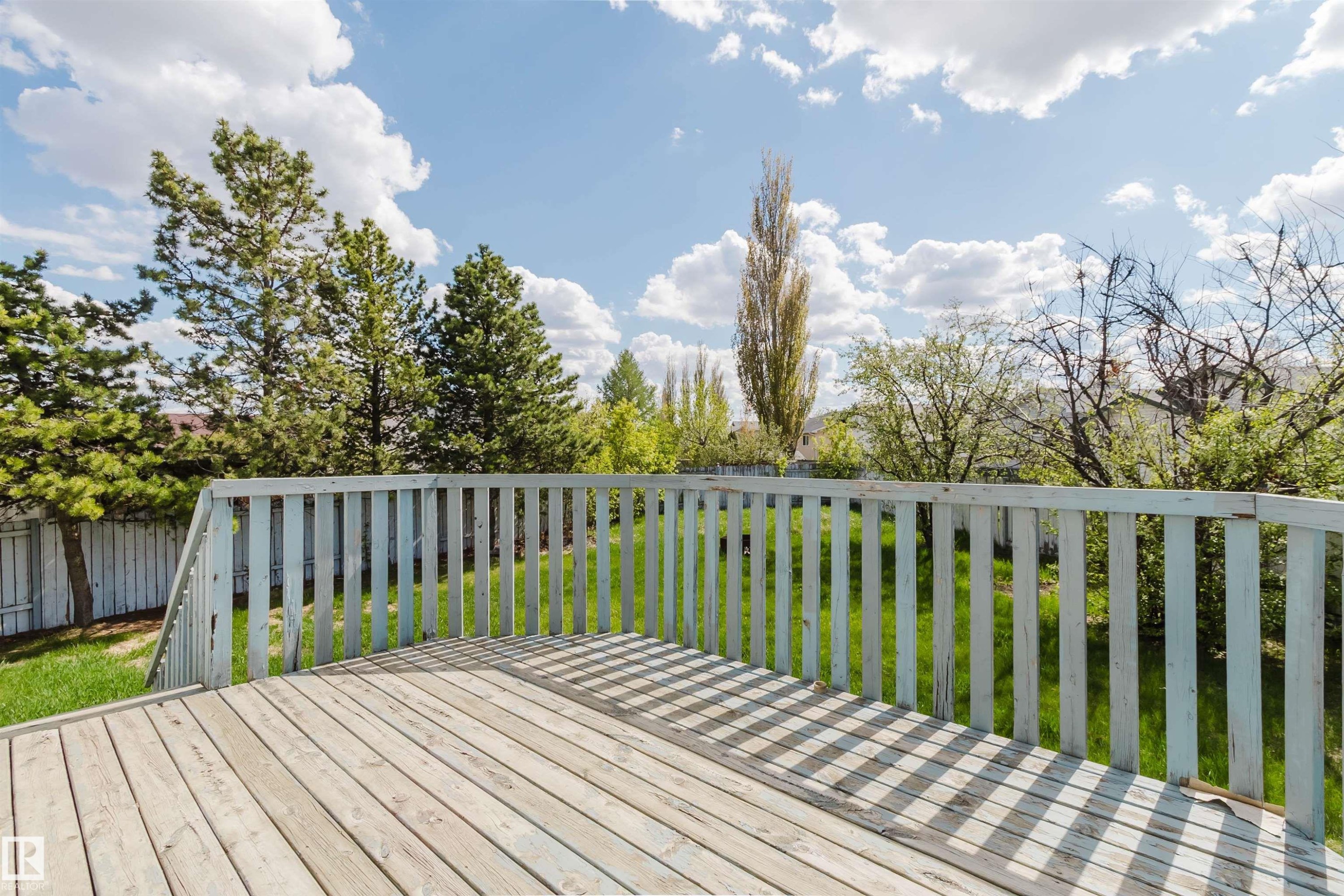 Expansive wood deck with a slatted railing, overlooking a green lawn and mature trees, enclosed by a wood fence - 13755 131B Avenue, Edmonton, AB - Outdoor With Deck Patio Veranda