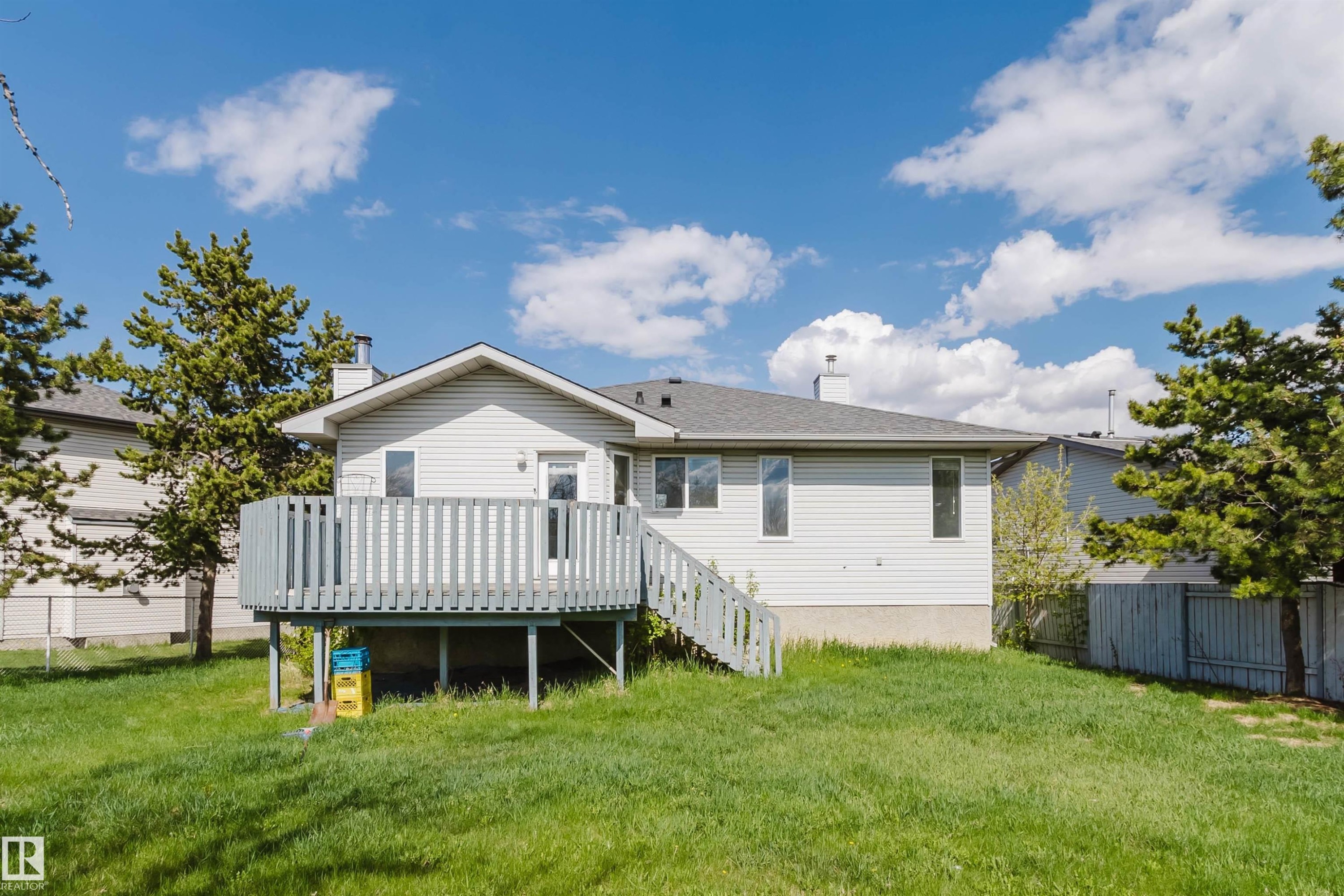 Spacious backyard featuring a light gray wood deck with coordinating railings and stairs, a manicured lawn, and mature evergreen trees - 13755 131B Avenue, Edmonton, AB - Outdoor