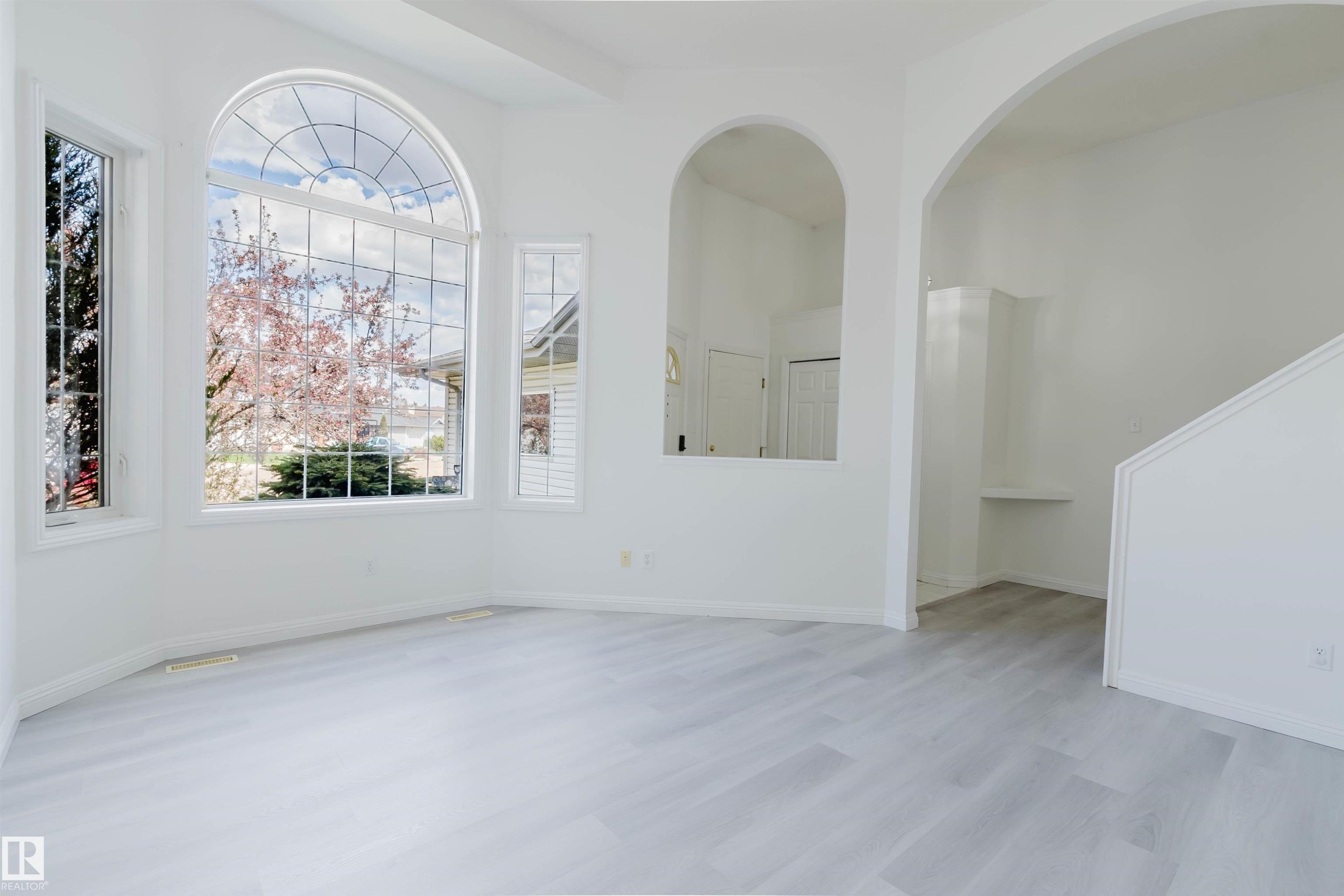 Bright interior space featuring a large arched window, additional tall windows, light wood-finish flooring, and white walls - 13755 131B Avenue, Edmonton, AB - Indoor Photo Showing Other Room