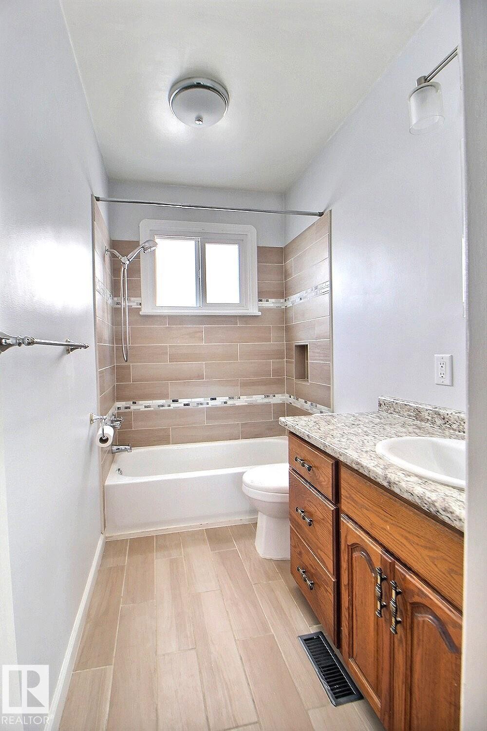 Bathroom featuring a built-in tub with tile surround, wood-finish flooring, a vanity with a countertop, and an integrated sink - 11626 87 Street Nw, Edmonton, AB - Indoor Photo Showing Bathroom