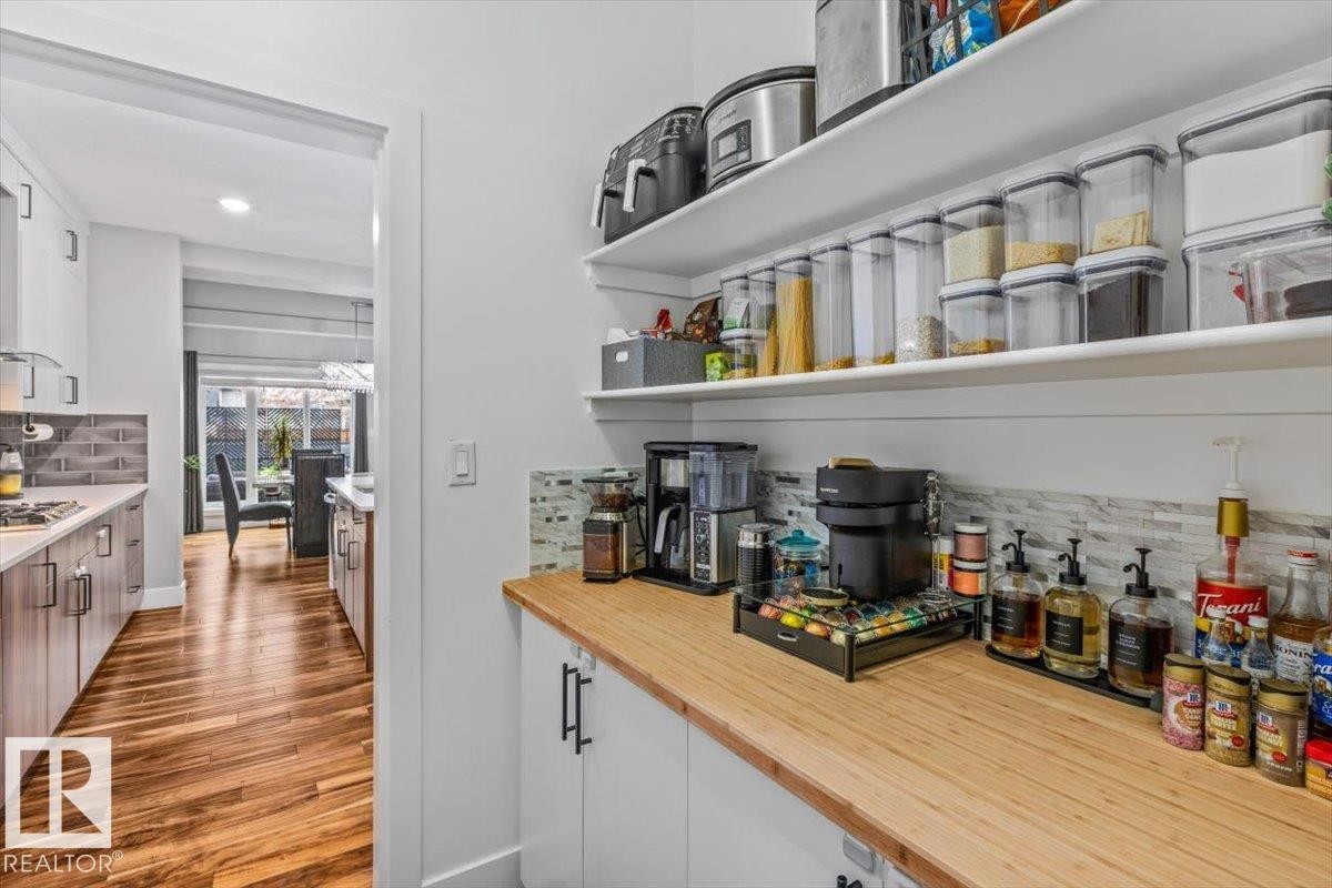 Dedicated pantry area featuring open shelving, a butcher block countertop, white cabinetry with black hardware, and a mosaic tile backsplash - 219 Cranberry Bend, Fort Saskatchewan, AB - Indoor Photo Showing Kitchen