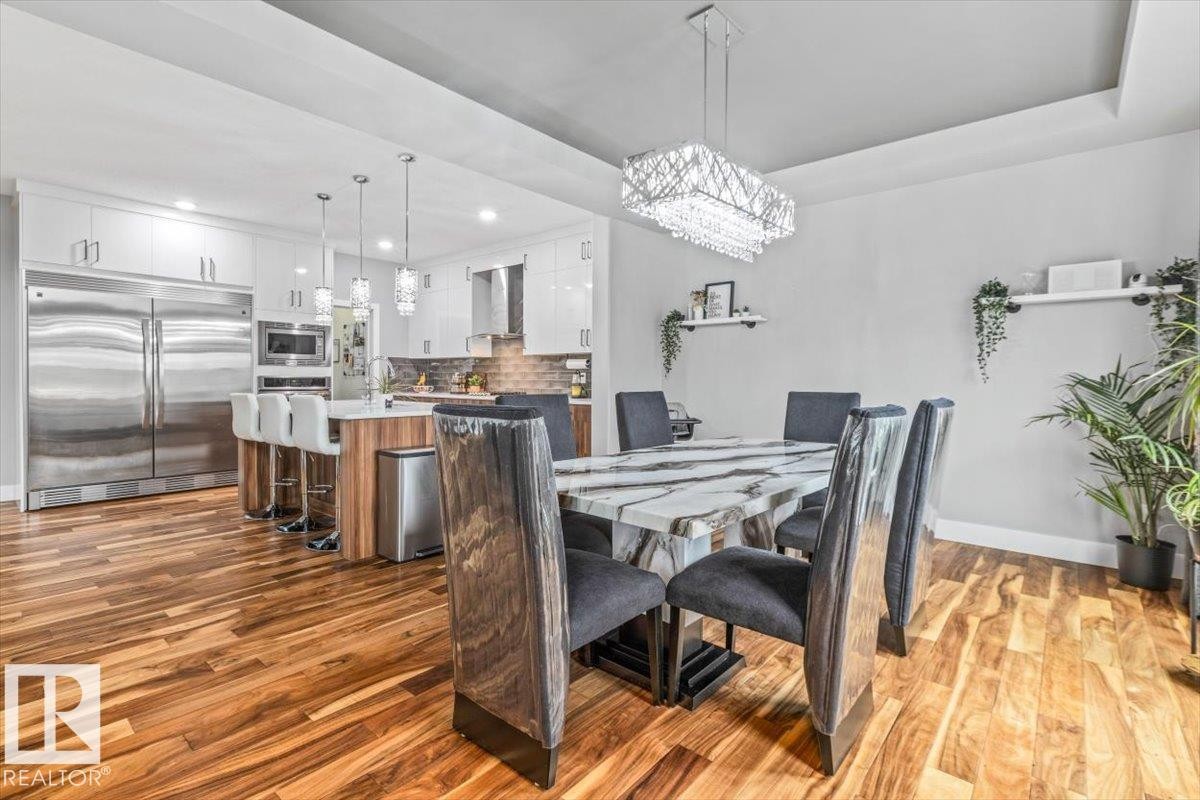 Open-concept dining area featuring wood-finish flooring, a contemporary chandelier, and a tray ceiling detail - 219 Cranberry Bend, Fort Saskatchewan, AB - Indoor Photo Showing Dining Room