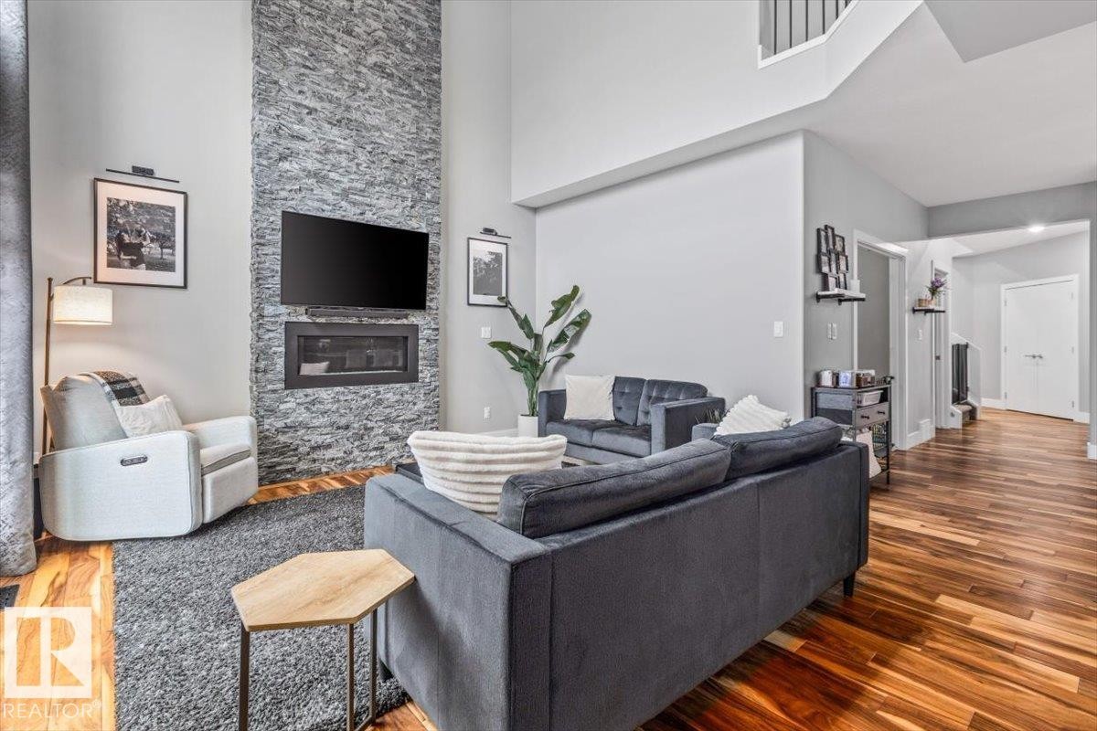 Living area featuring a floor-to-ceiling stacked stone fireplace, a wall-mounted media center, and high ceilings - 219 Cranberry Bend, Fort Saskatchewan, AB - Indoor Photo Showing Living Room With Fireplace