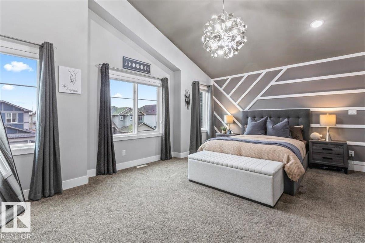 Vaulted ceiling bedroom featuring a textured accent wall, plush carpet flooring, and two large windows with dark curtains - 219 Cranberry Bend, Fort Saskatchewan, AB - Indoor Photo Showing Bedroom