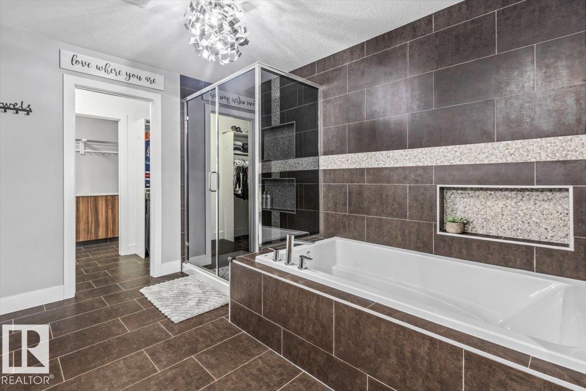 Bathroom featuring dark tile flooring, a built-in soaking tub with dark tile surround, and a glass-enclosed shower with contrasting wall tile - 219 Cranberry Bend, Fort Saskatchewan, AB - Indoor Photo Showing Bathroom