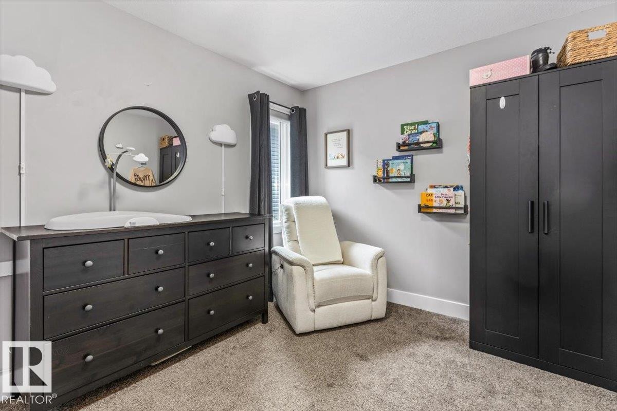 Neutral-toned room featuring a dark wood-finish dresser with nine drawers, a round wall mirror, and a window with dark draperies - 219 Cranberry Bend, Fort Saskatchewan, AB - Indoor