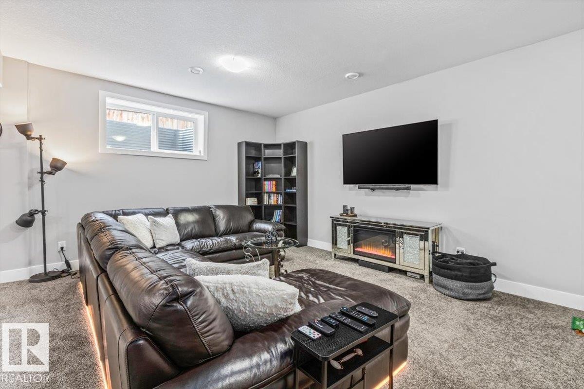 Carpeted room with a wall-mounted television, an electric fireplace with a mirrored surround, a built-in corner bookshelf, and a horizontal window - 219 Cranberry Bend, Fort Saskatchewan, AB - Indoor Photo Showing Living Room With Fireplace