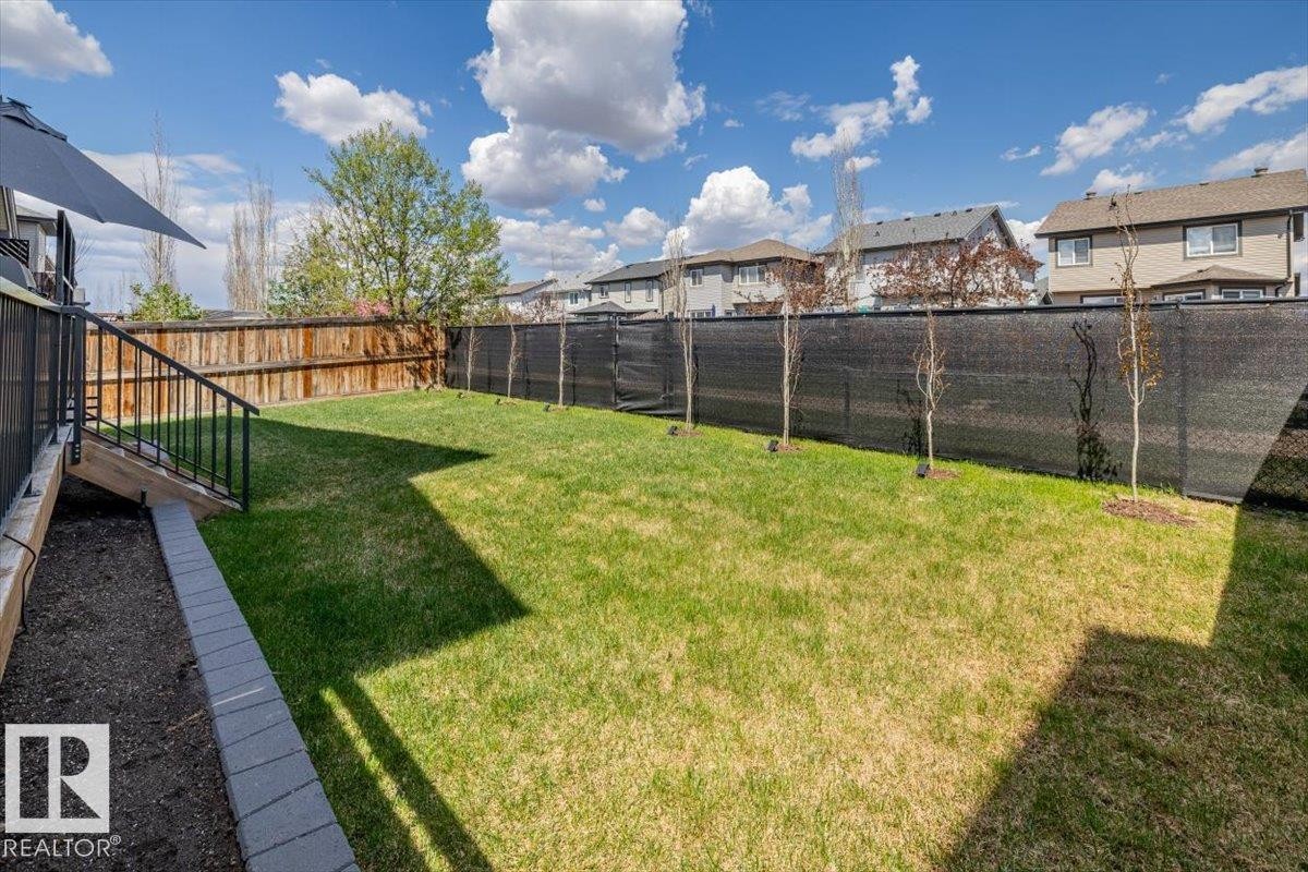 Expansive backyard featuring a lush lawn, wooden privacy fencing, and a deck with dark metal railings - 219 Cranberry Bend, Fort Saskatchewan, AB - Outdoor