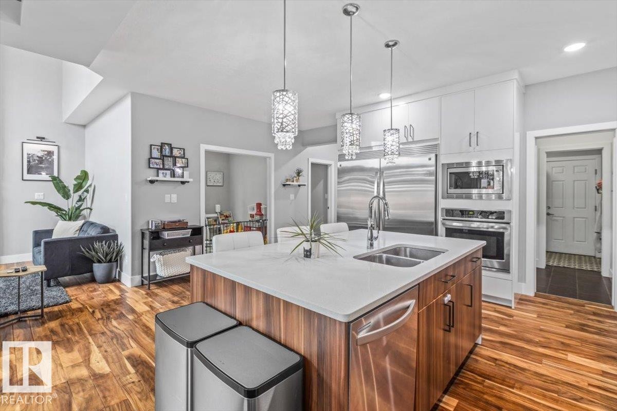 Open-concept kitchen featuring a large island with white countertop, integrated double sink with gooseneck faucet, and wood-finish cabinetry - 219 Cranberry Bend, Fort Saskatchewan, AB - Indoor Photo Showing Kitchen With Double Sink With Upgraded Kitchen