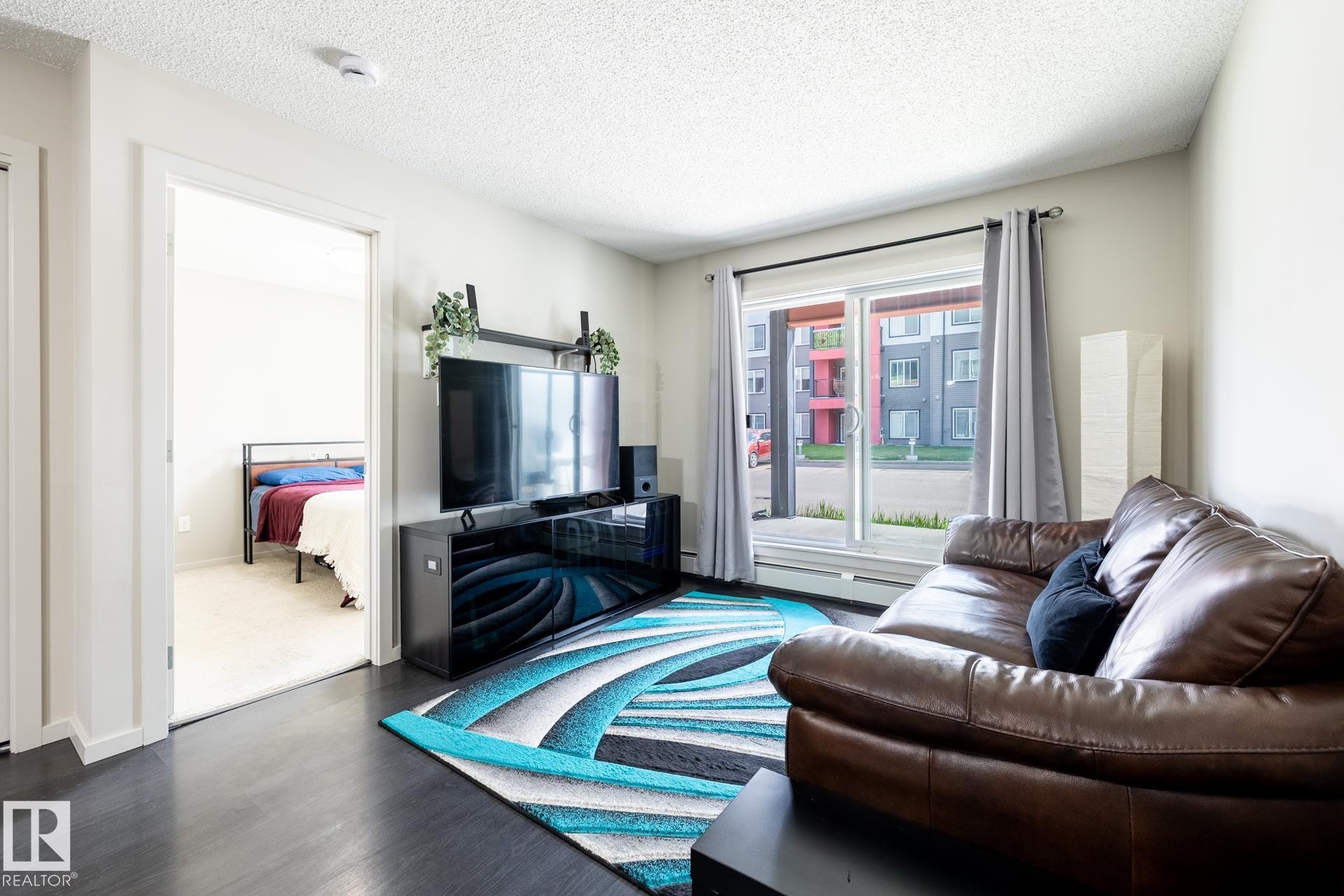Living area featuring dark wood-finish flooring, light-toned walls, and a sliding glass door - 131 344 Windermere Road, Edmonton, AB - Indoor Photo Showing Living Room