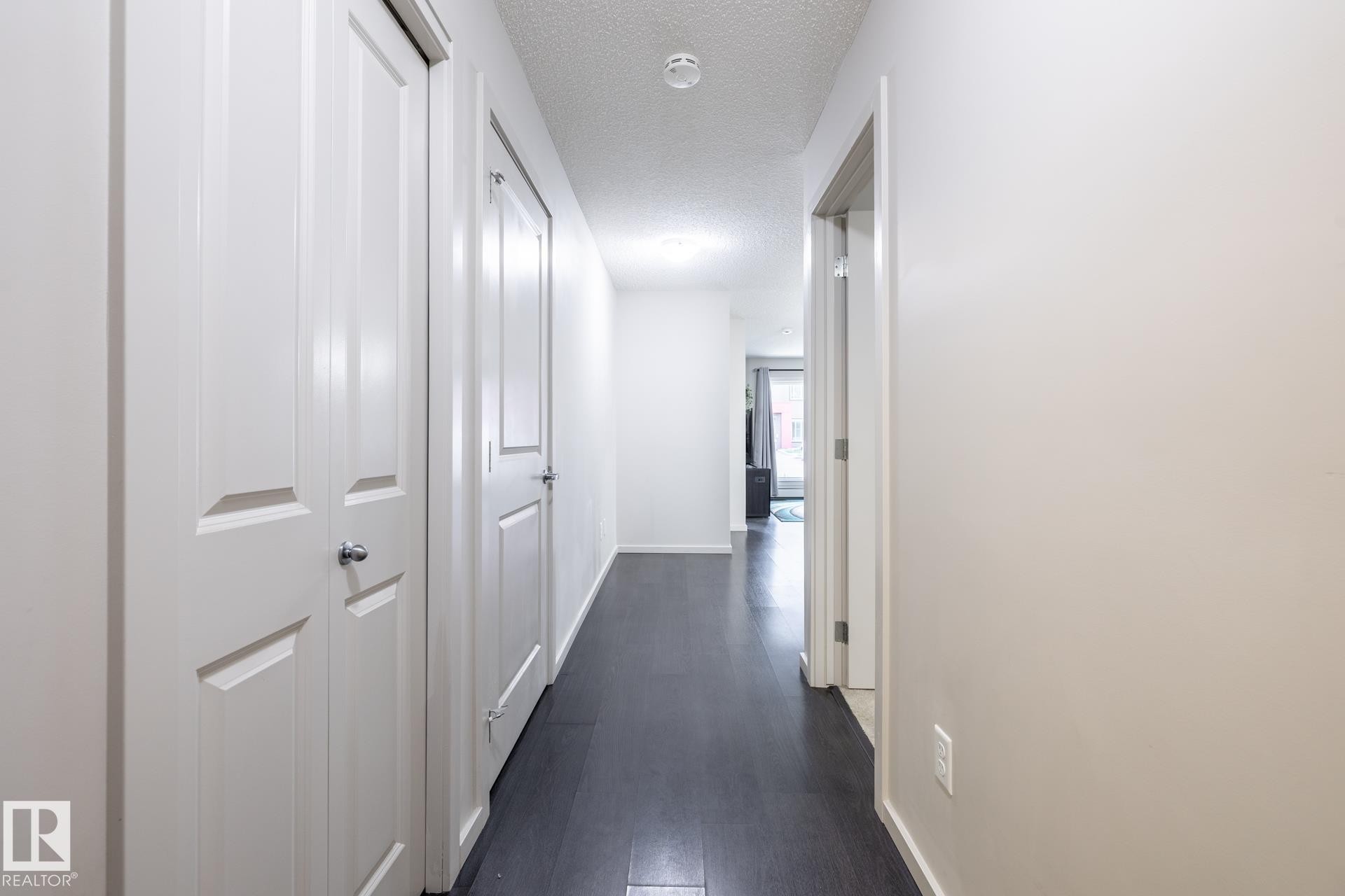 Entryway corridor featuring dark wood-finish flooring, light-colored walls, and white paneled doors - 131 344 Windermere Road, Edmonton, AB - Indoor Photo Showing Other Room