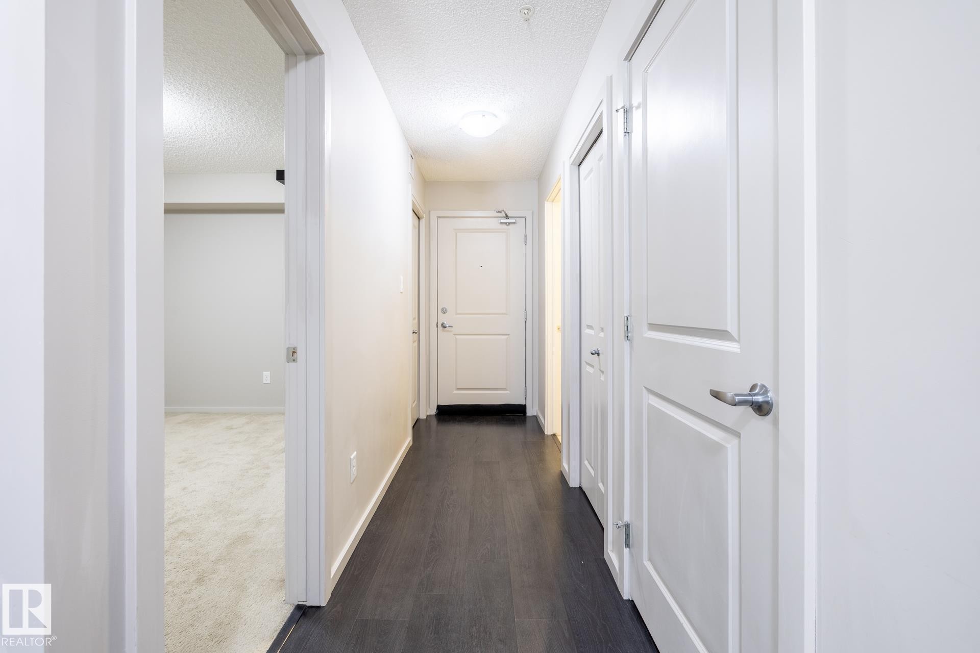 Hallway featuring dark wood-finish flooring, light-colored walls, and multiple panel doors - 131 344 Windermere Road, Edmonton, AB - Indoor Photo Showing Other Room