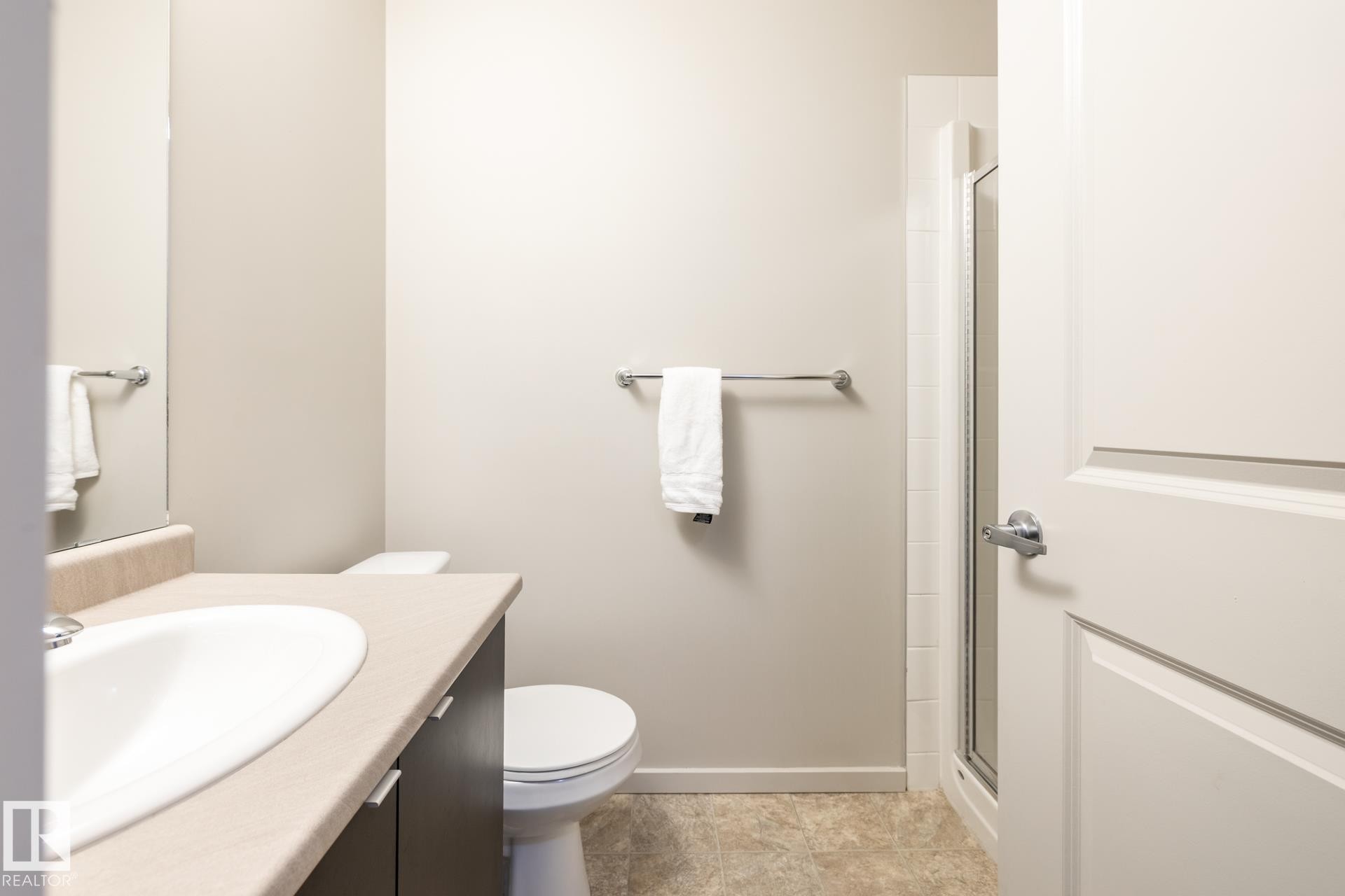 Bathroom featuring a dark wood-finish vanity with a light countertop, an undermount sink, and a glass-enclosed shower - 131 344 Windermere Road, Edmonton, AB - Indoor Photo Showing Bathroom