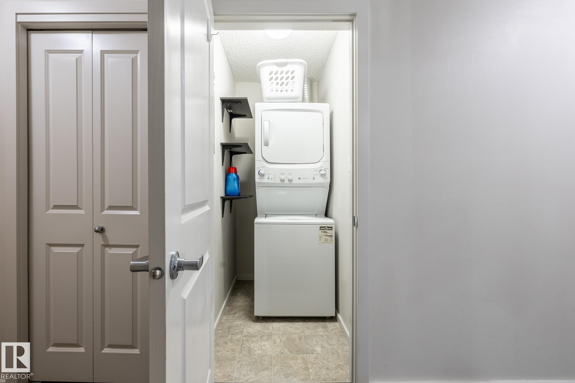 Dedicated laundry closet featuring a stackable washer and dryer unit, built-in shelving, and light-toned floor tile - 131 344 Windermere Road, Edmonton, AB - Indoor Photo Showing Laundry Room
