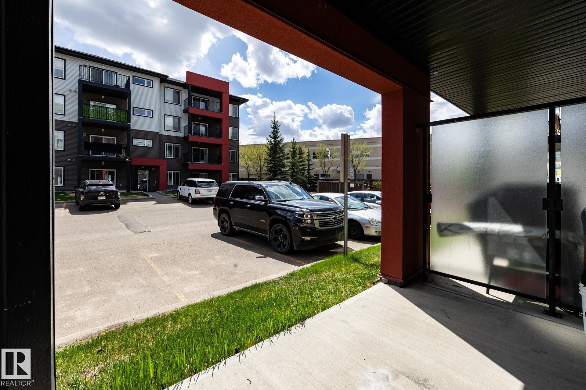 Multi-story residential building with modern exterior finishes, private balconies, and an adjacent parking area - 131 344 Windermere Road, Edmonton, AB - Outdoor