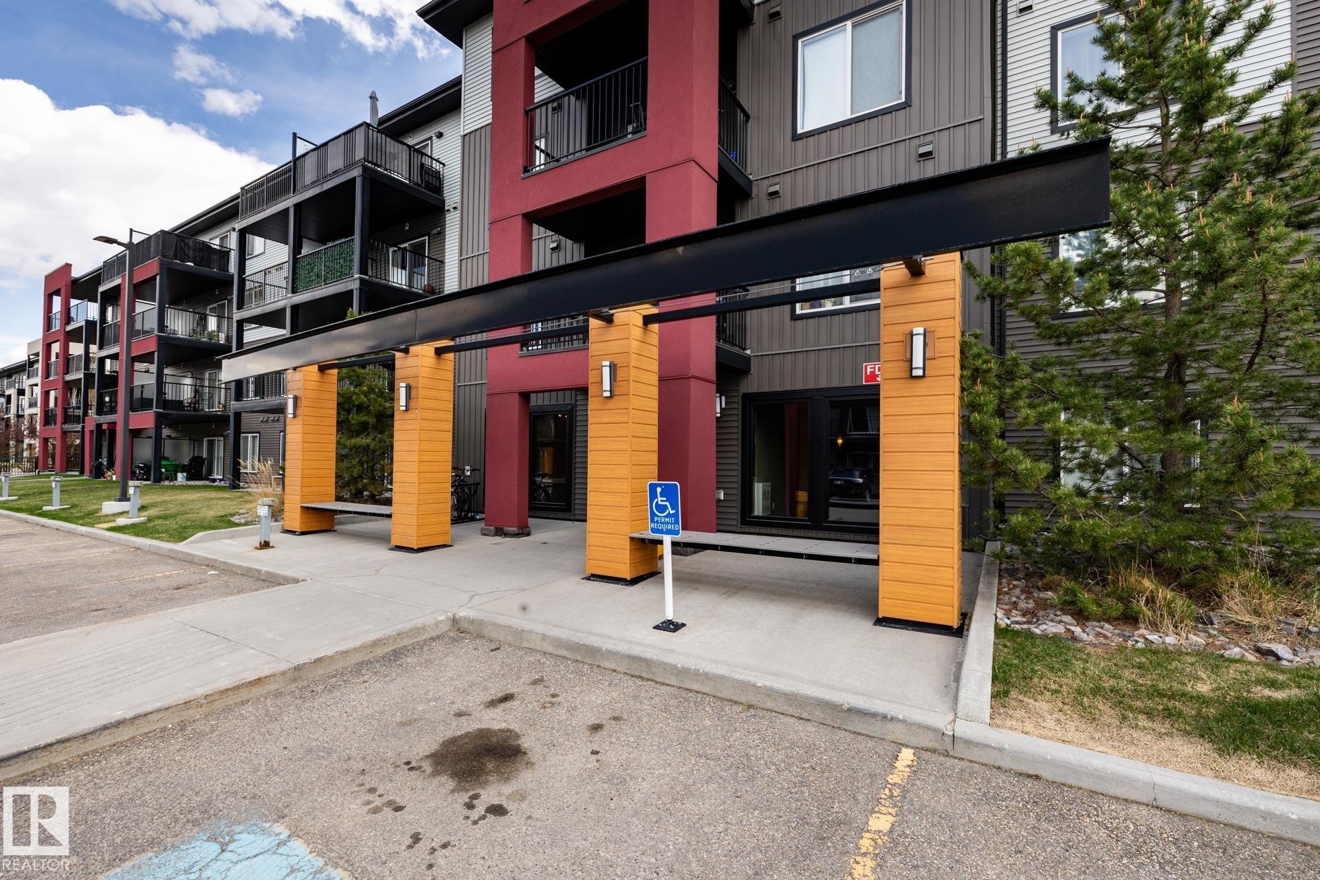 Building exterior featuring a covered entryway with wood-panel accents and modern wall sconces - 131 344 Windermere Road, Edmonton, AB - Outdoor