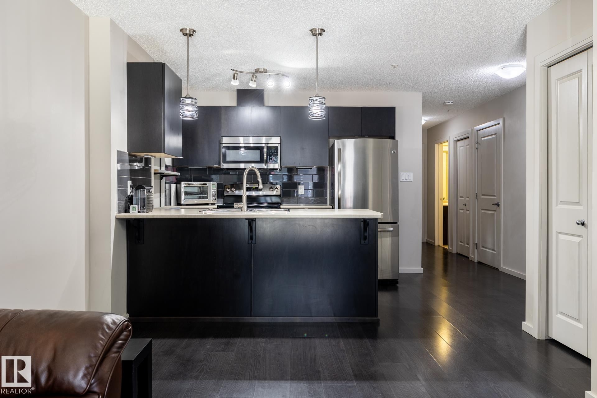 Modern kitchen featuring dark cabinetry, stainless steel appliances, and a light-toned countertop - 131 344 Windermere Road, Edmonton, AB - Indoor Photo Showing Kitchen With Upgraded Kitchen