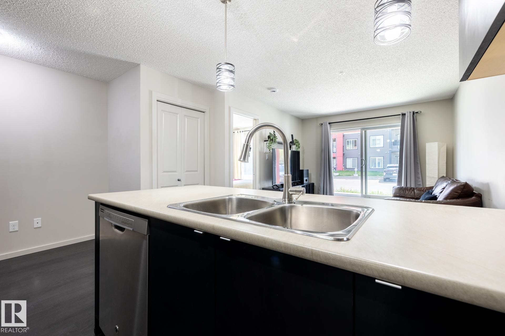 Kitchen island featuring a double basin stainless steel sink, a pull-down faucet, and a built-in dishwasher - 131 344 Windermere Road, Edmonton, AB - Indoor Photo Showing Kitchen With Double Sink