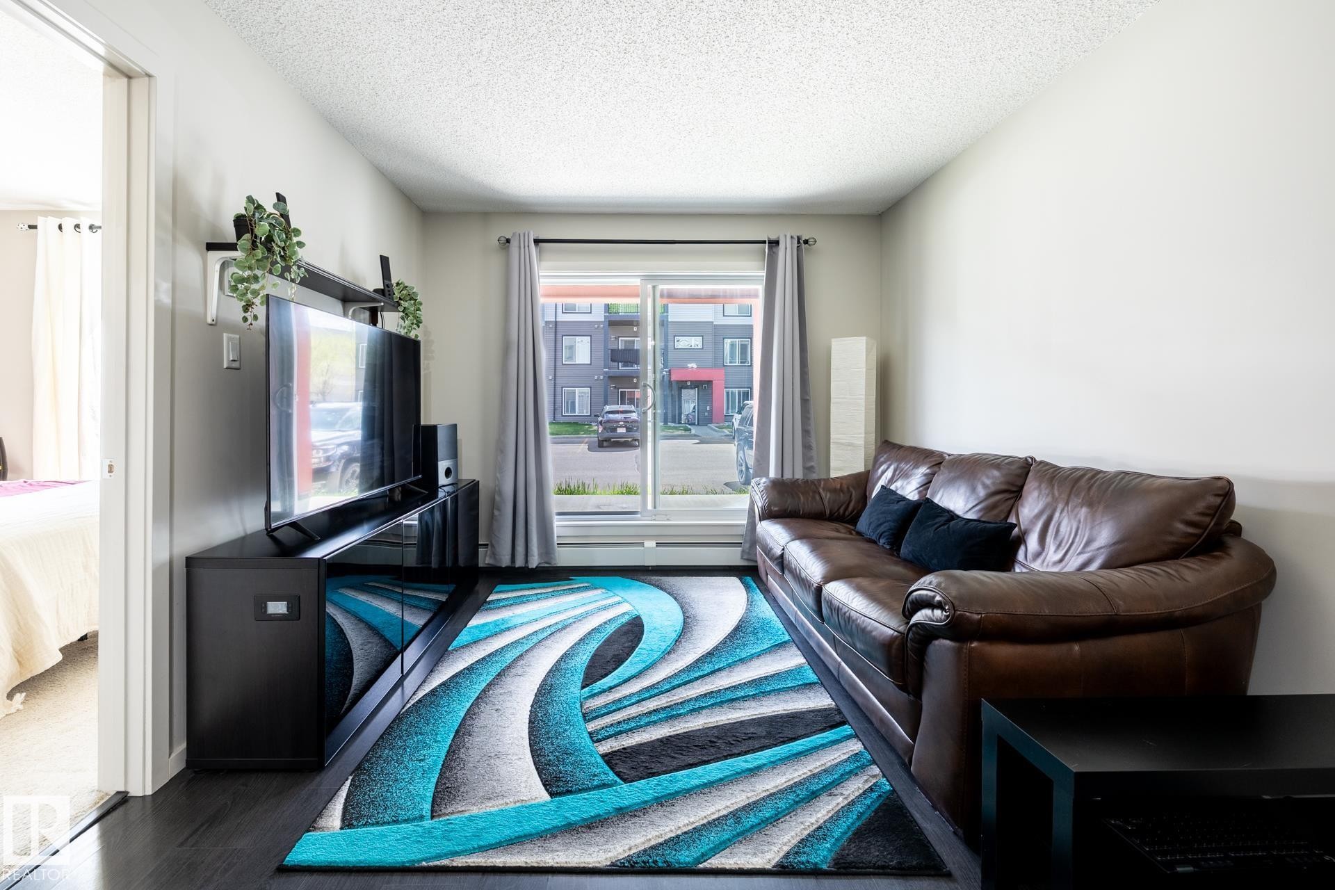 Dark wood-finish flooring complements light-toned walls - 131 344 Windermere Road, Edmonton, AB - Indoor Photo Showing Living Room