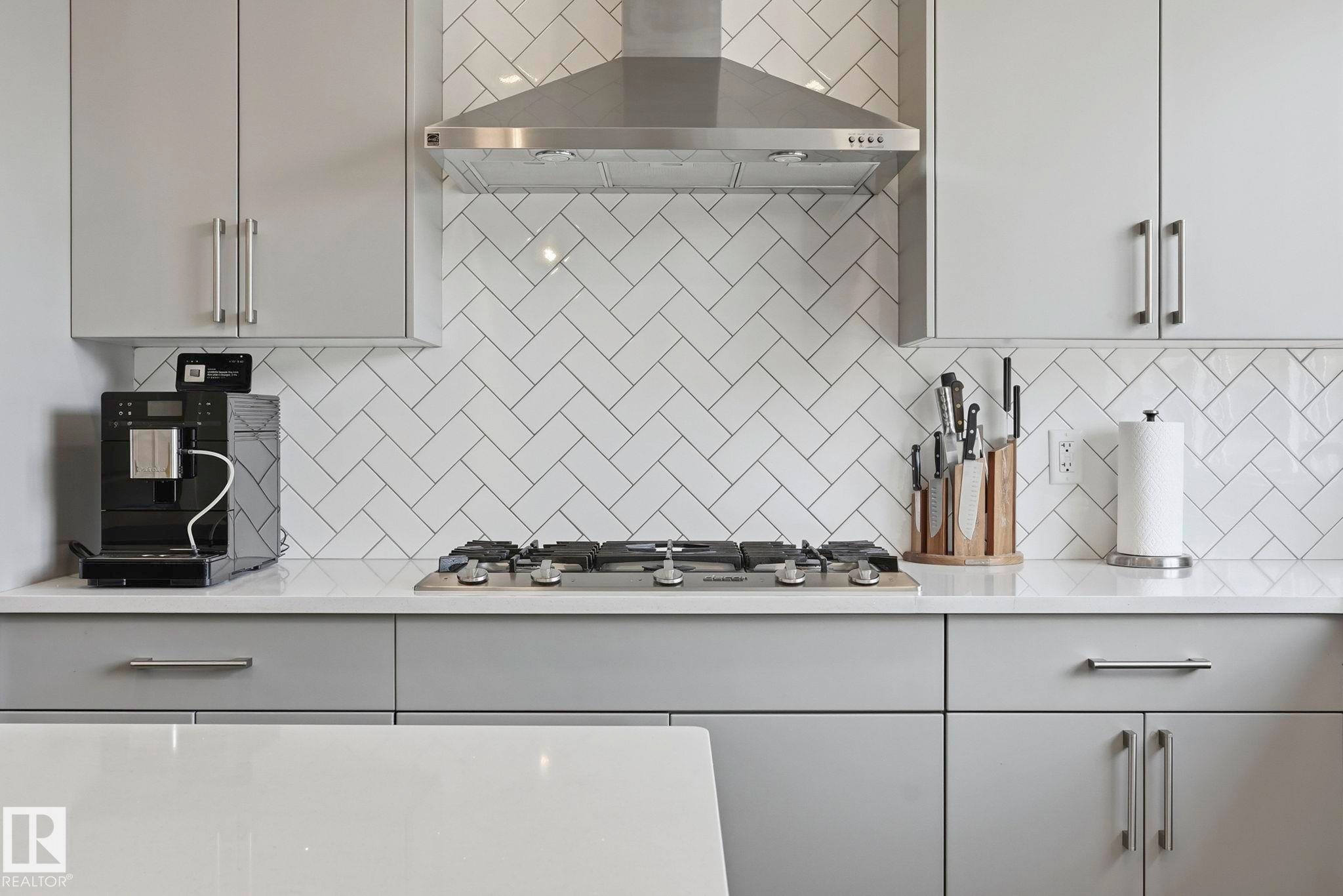 Contemporary kitchen featuring light gray cabinetry, a white herringbone tile backsplash, and a stainless steel range hood - 2116 159 Street, Edmonton, AB - Indoor Photo Showing Kitchen With Upgraded Kitchen