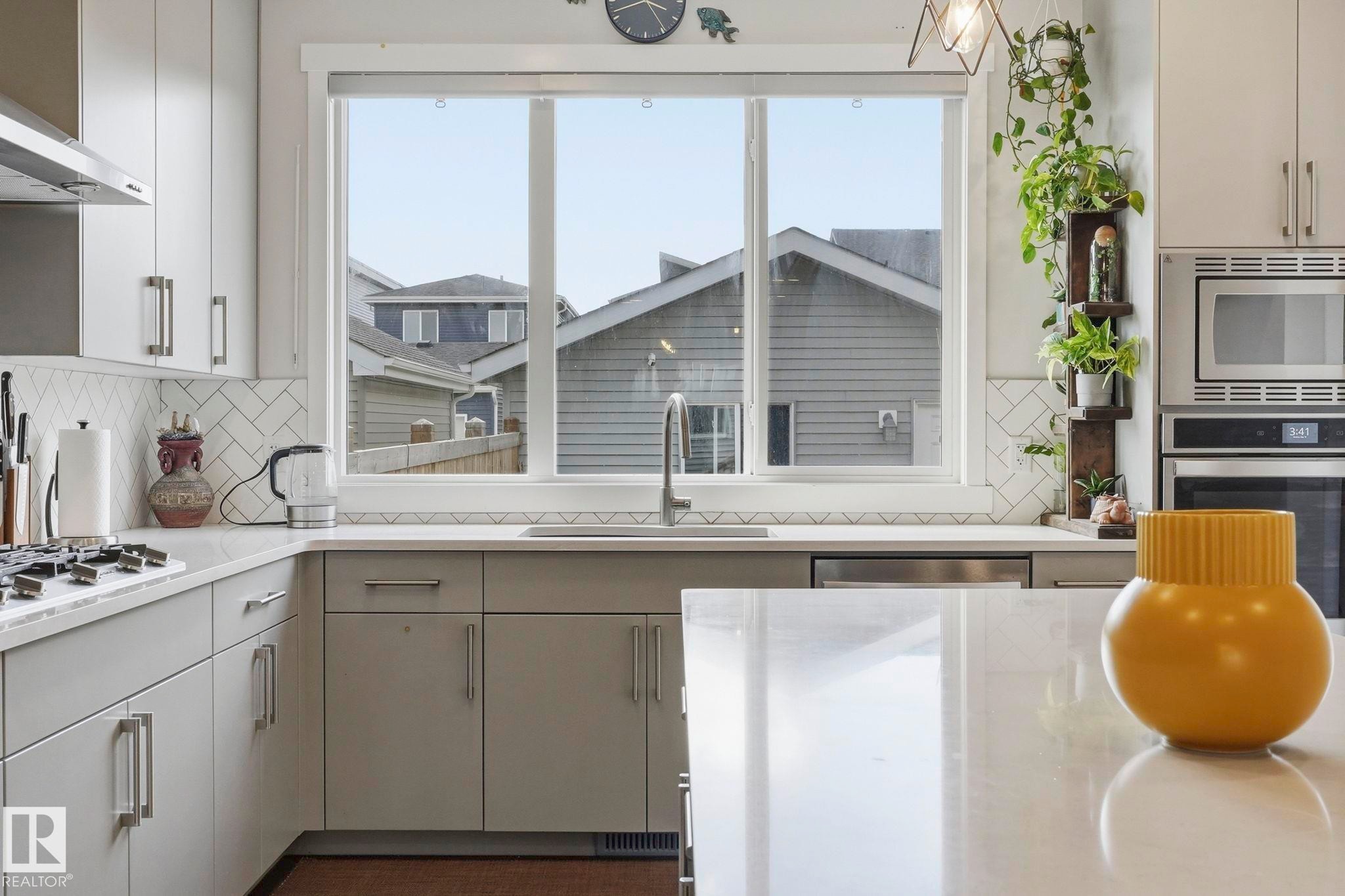 Modern kitchen featuring light gray cabinetry with brushed nickel hardware, white stone-finish countertops, and a full-height herringbone tile backsplash - 2116 159 Street, Edmonton, AB - Indoor Photo Showing Kitchen With Upgraded Kitchen