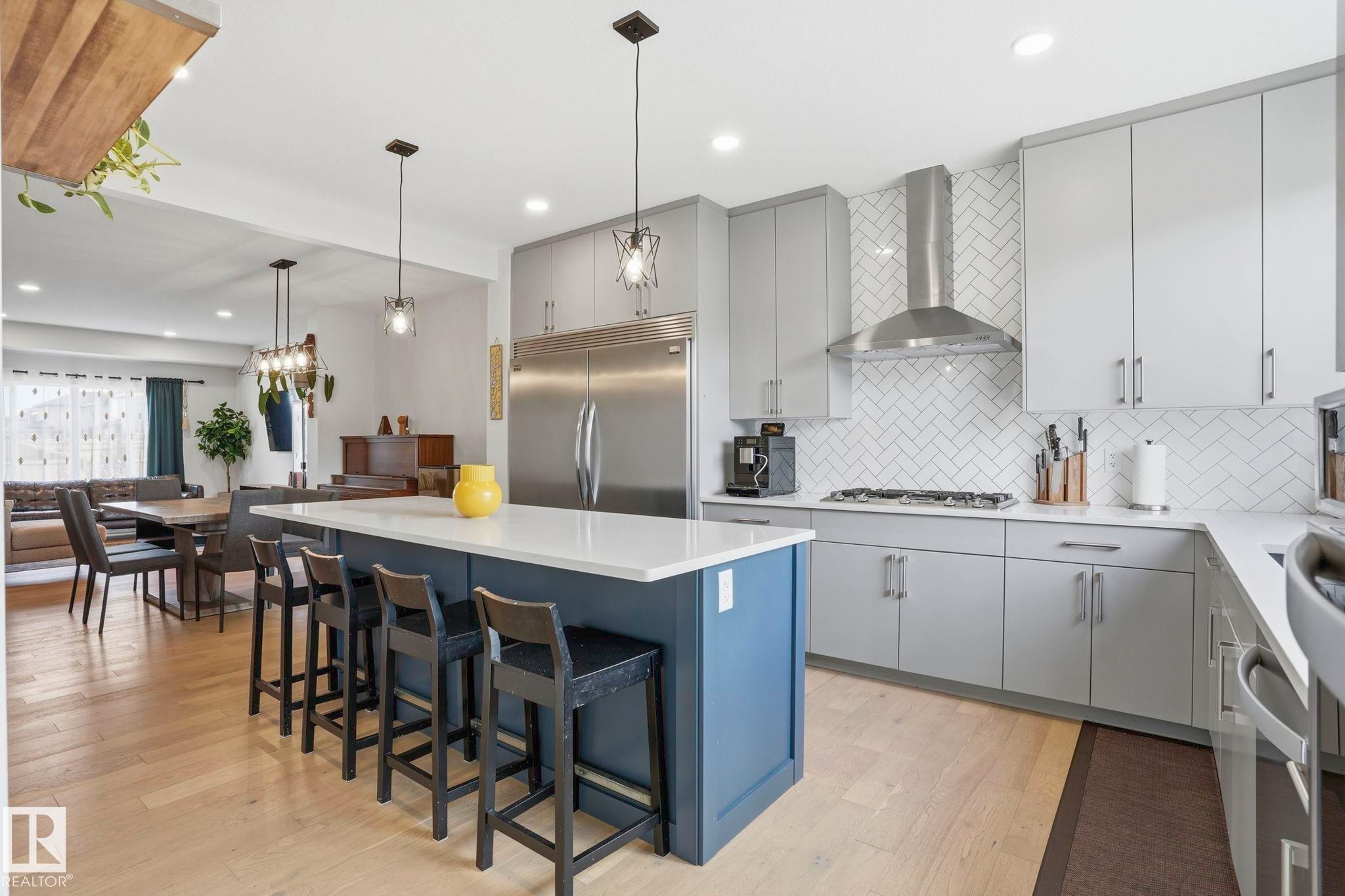 Modern kitchen featuring light gray cabinetry, stainless steel appliances, a white herringbone tile backsplash, and a blue island with a white countertop - 2116 159 Street, Edmonton, AB - Indoor Photo Showing Kitchen With Upgraded Kitchen