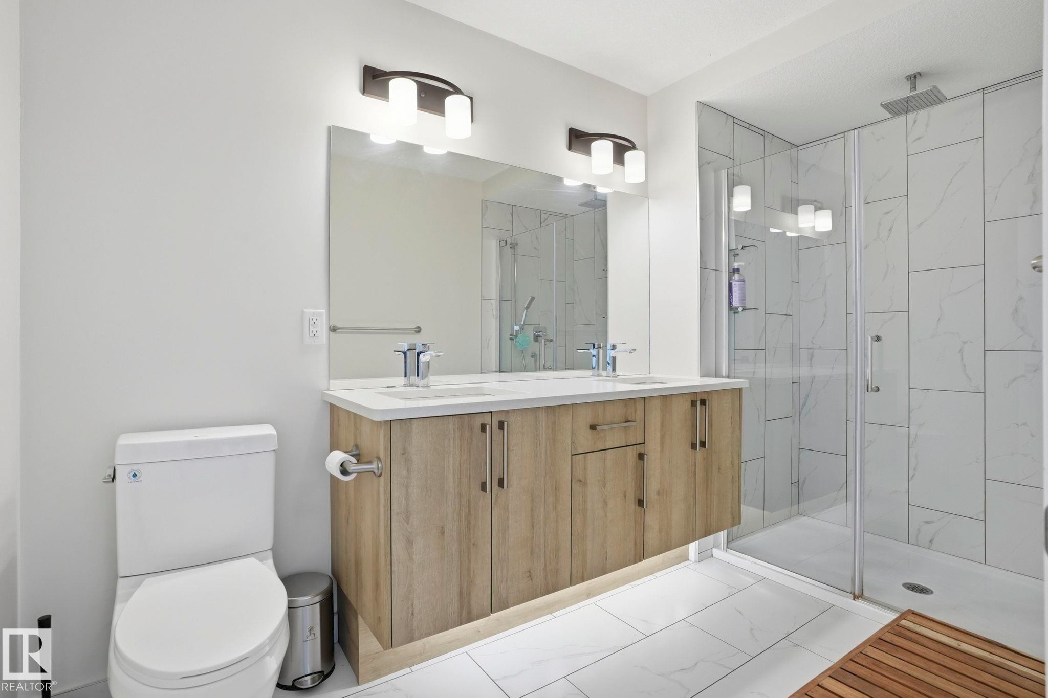 Bathroom featuring a dual-sink vanity with wood-finish cabinetry and a light-toned countertop, a frameless glass shower enclosure with floor-to-ceiling tile, a square rain shower head, and tile flooring - 2116 159 Street, Edmonton, AB - Indoor Photo Showing Bathroom