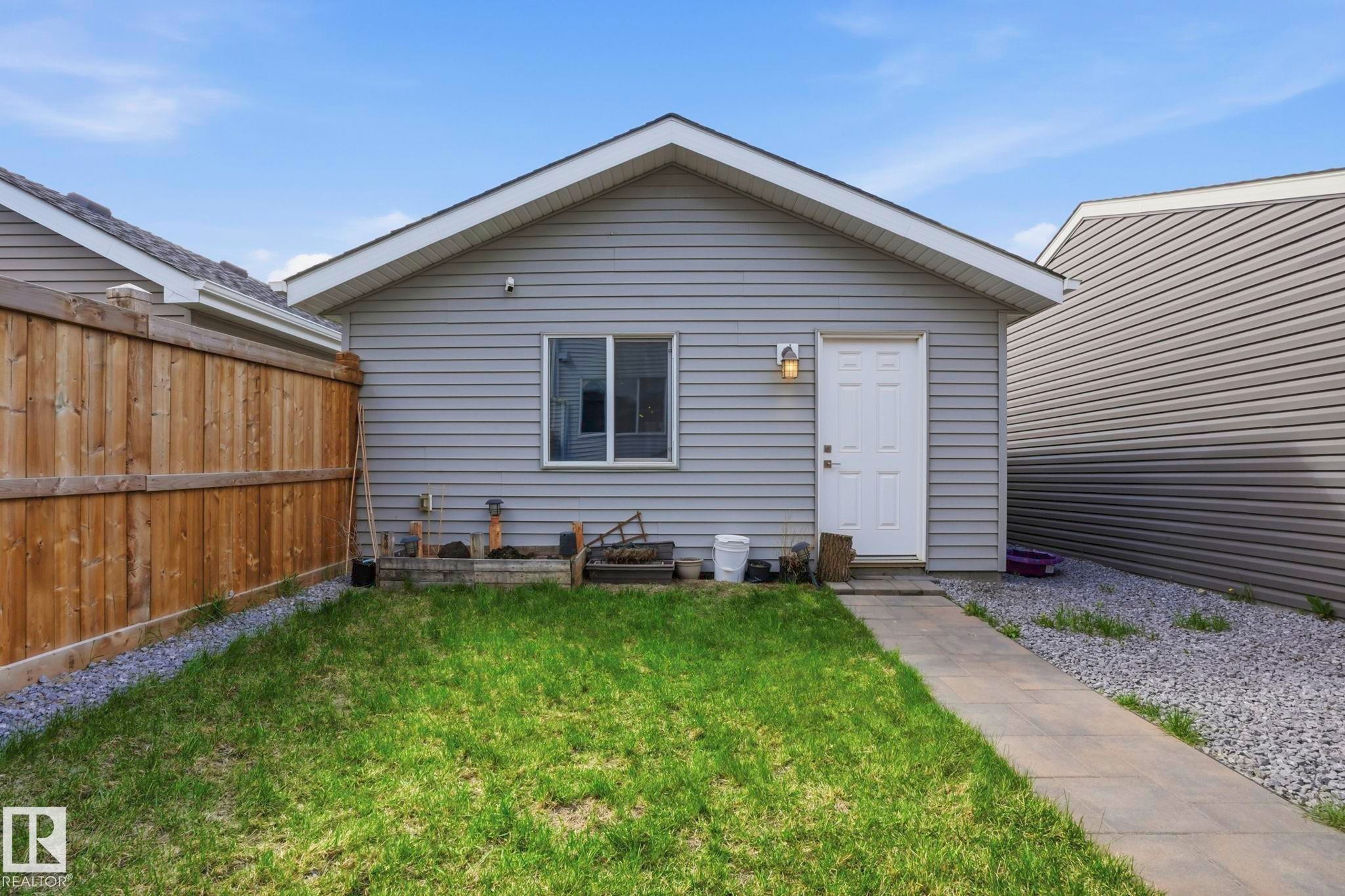 Detached gray siding structure featuring a white entry door, exterior wall lantern, and a single window - 2116 159 Street, Edmonton, AB - Outdoor With Exterior