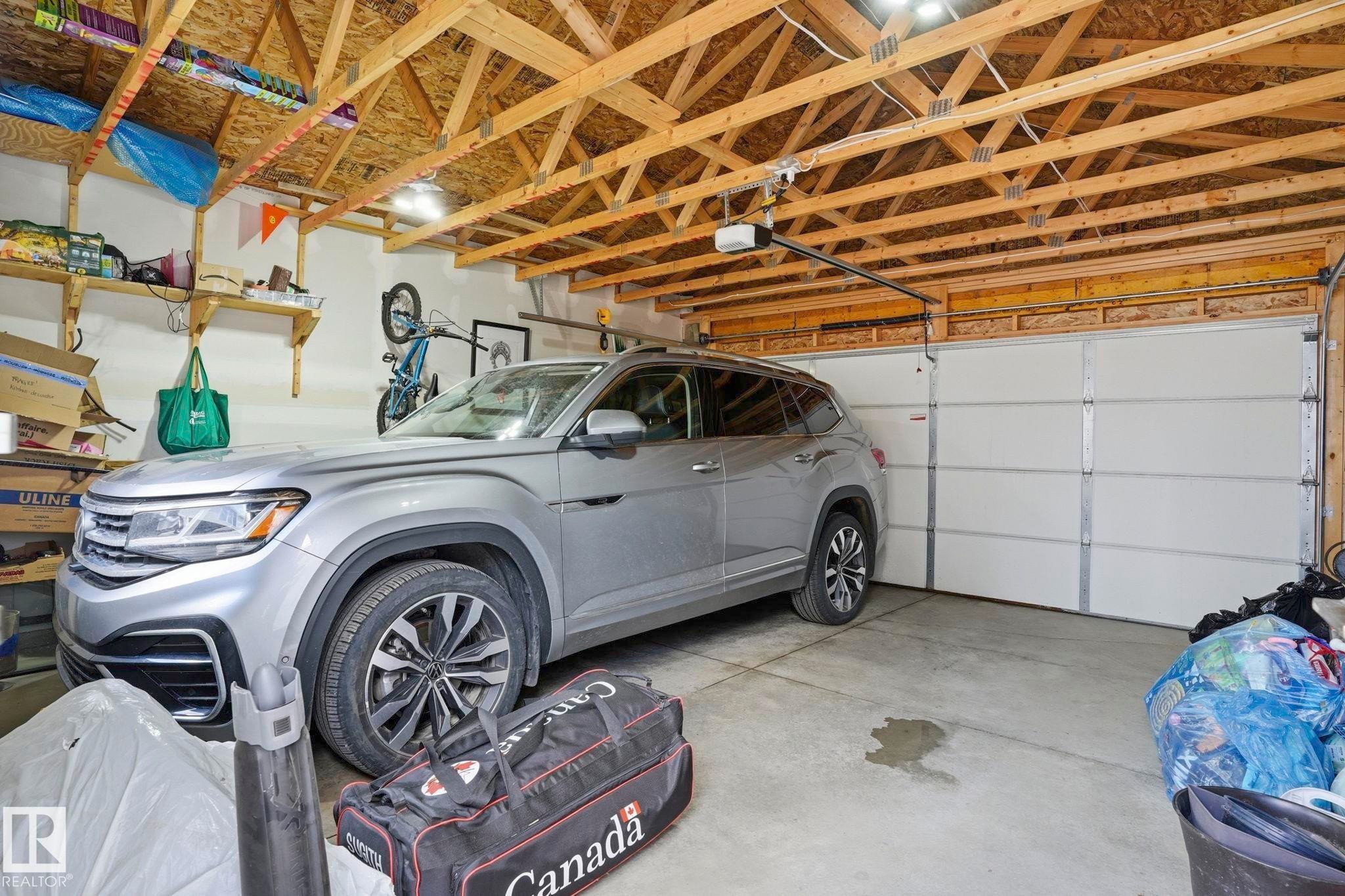 Attached garage with an overhead door, exposed wood ceiling joists, and a concrete floor - 2116 159 Street, Edmonton, AB - Indoor Photo Showing Garage