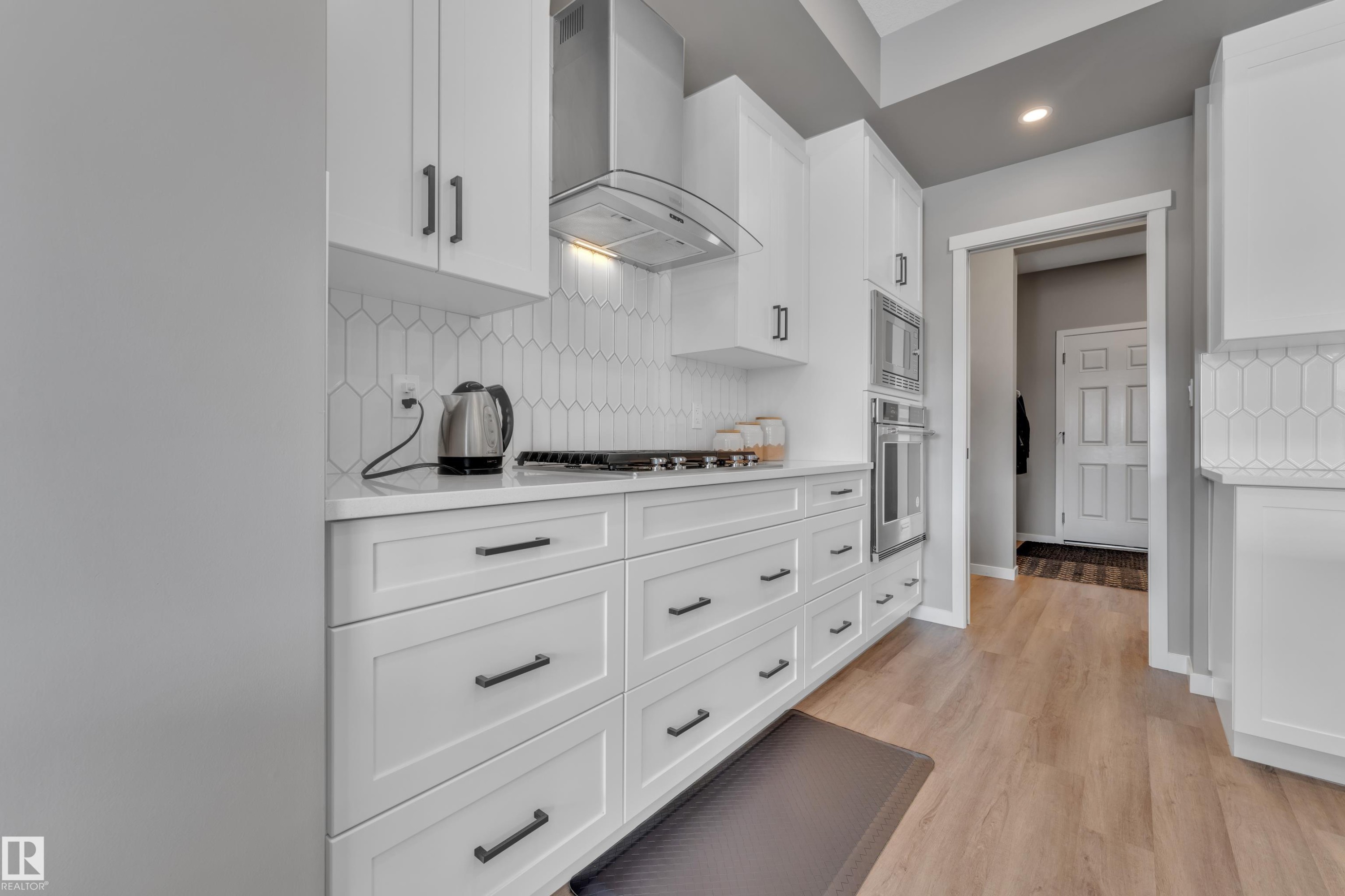The kitchen features white cabinetry with dark hardware, a white tiled backsplash, and stainless steel appliances including a range hood and double oven - 21853 98A Avenue, Edmonton, AB - Indoor Photo Showing Kitchen