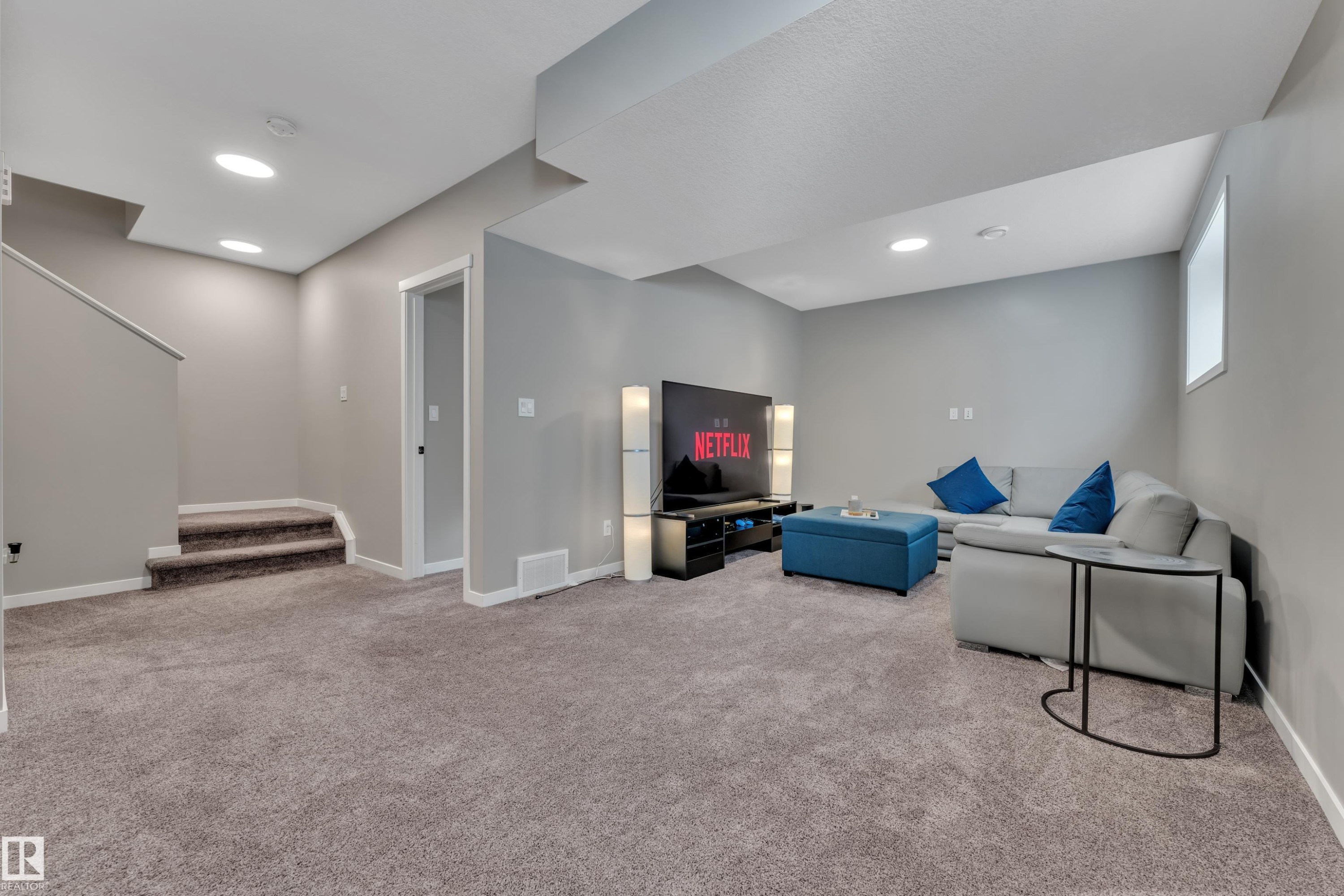 Expansive carpeted living area featuring recessed lighting, a window providing natural light, and a staircase with carpeted steps - 21853 98A Avenue, Edmonton, AB - Indoor