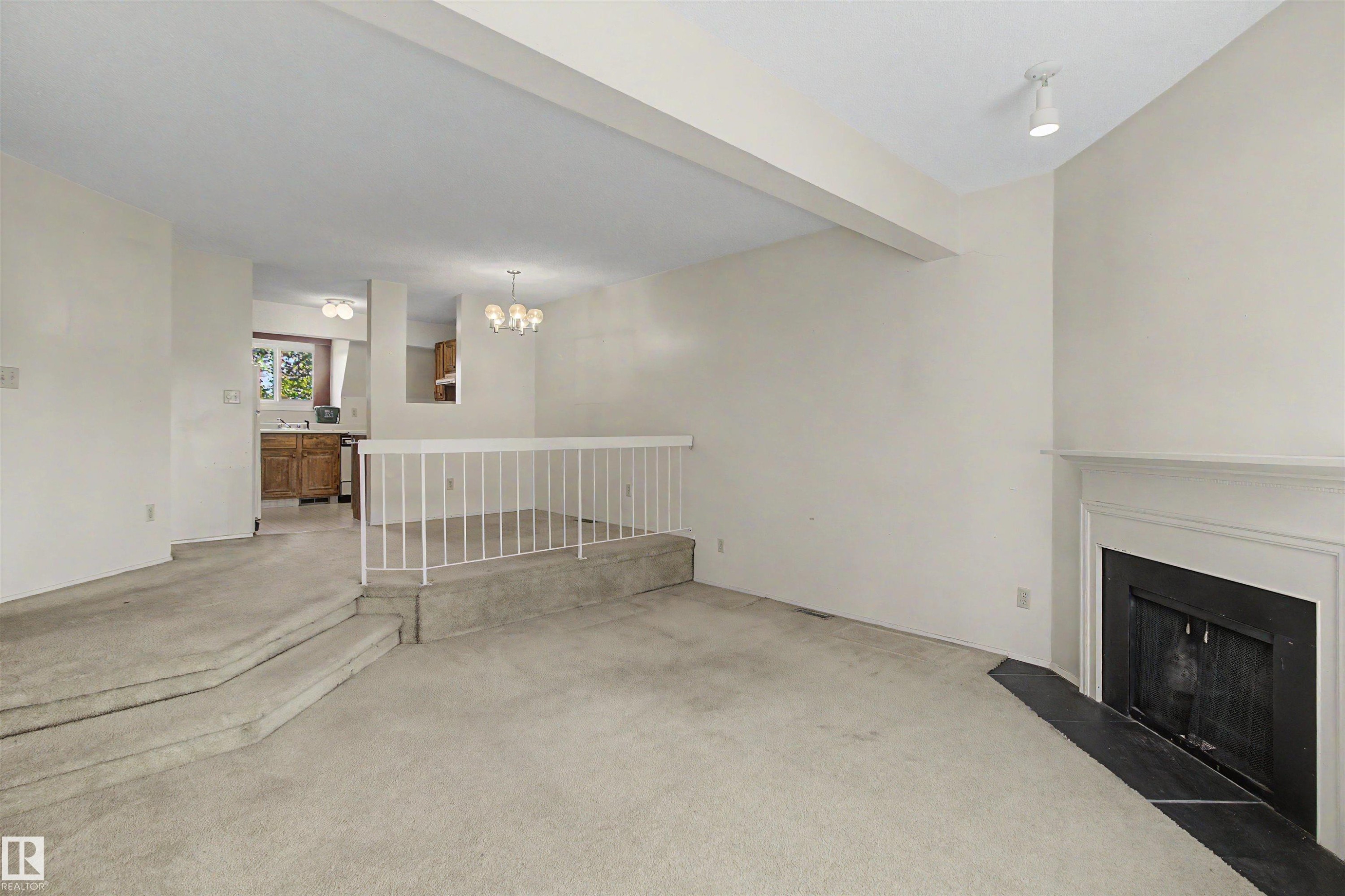 Living area featuring a fireplace with a white mantel and dark hearth, track lighting, and carpeted flooring - 5953 40 Avenue, Edmonton, AB