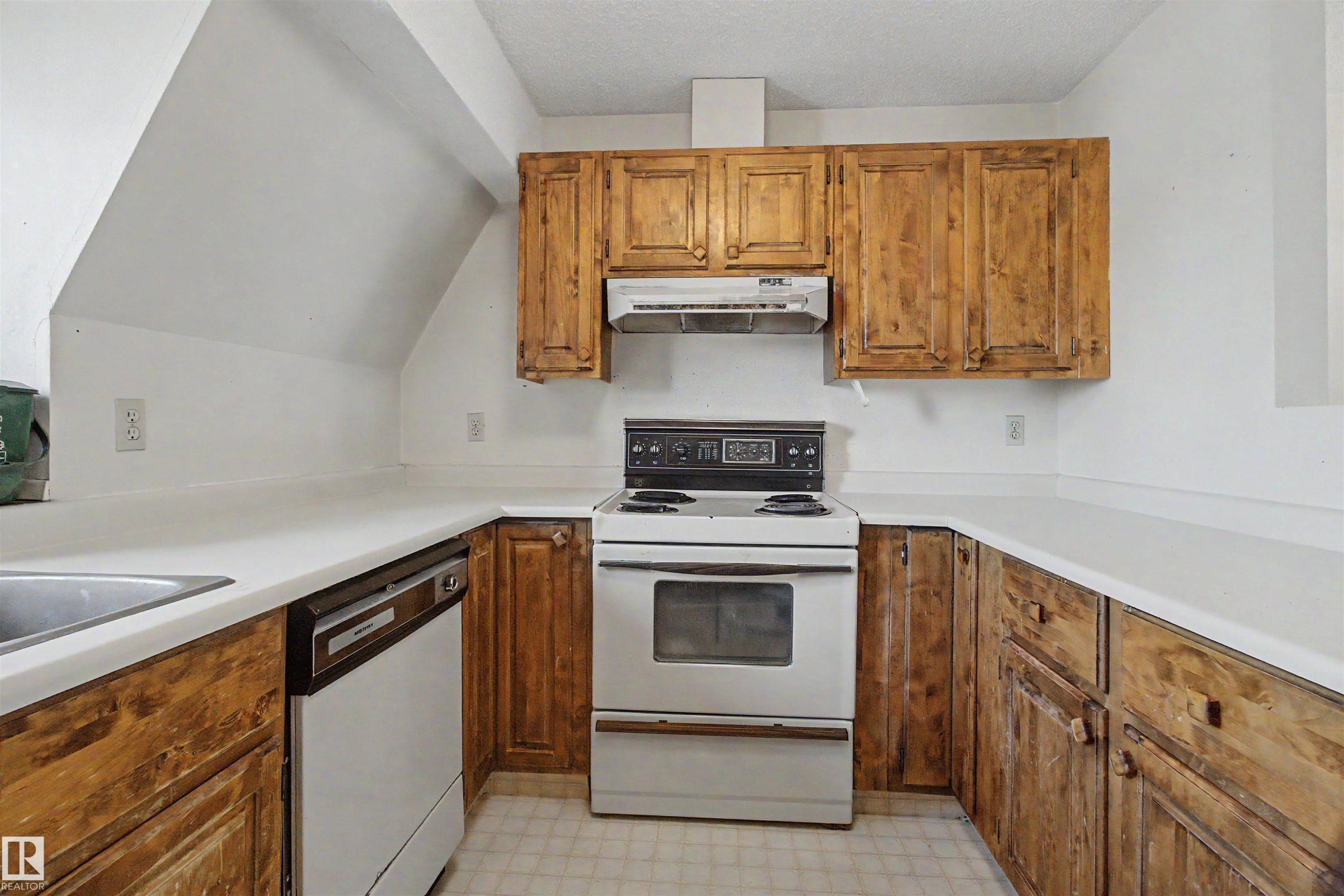 U-shaped kitchen layout featuring wood cabinetry, white countertops, and a built-in dishwasher - 5953 40 Avenue, Edmonton, AB