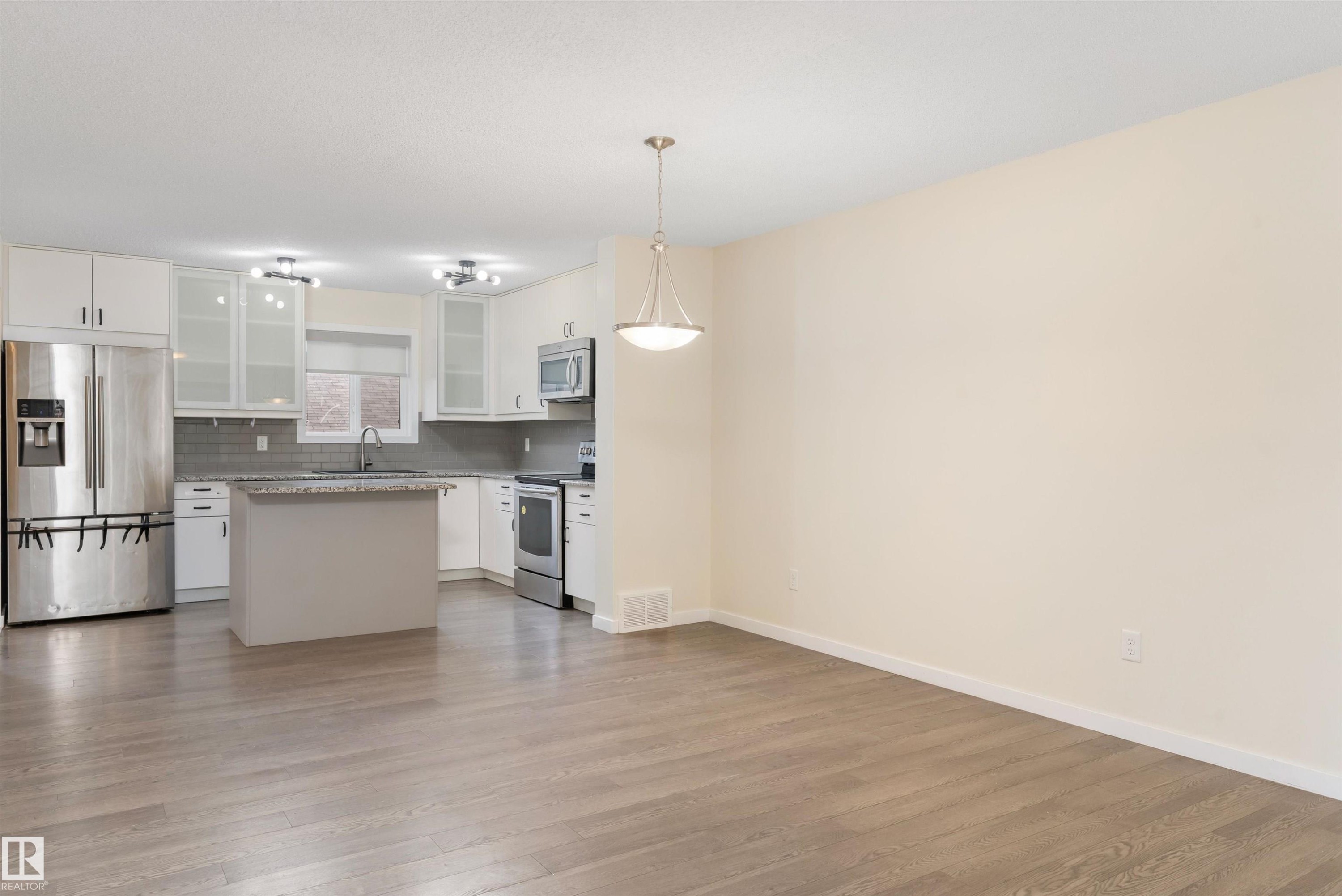 Open-concept kitchen and living area featuring wood-finish flooring, white cabinetry, stainless steel appliances, a center island, and a pendant light fixture - 336 Watt Boulevard, Edmonton, AB - Indoor Photo Showing Kitchen