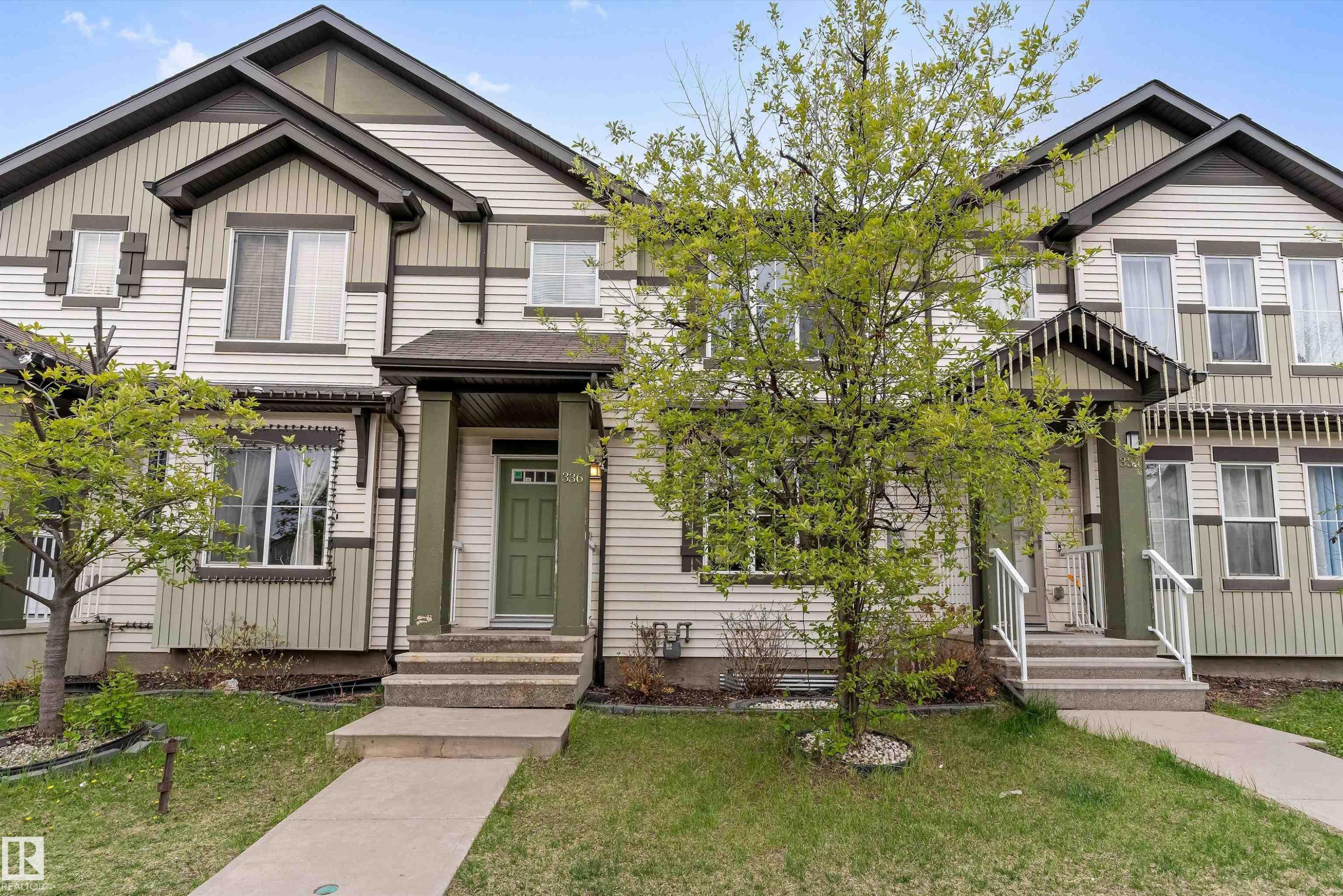 Multi-level townhouse facade featuring light-colored siding with contrasting trim, a covered entryway with a green door, multiple windows, and a concrete pathway leading to the entrance - 336 Watt Boulevard, Edmonton, AB - Outdoor With Facade