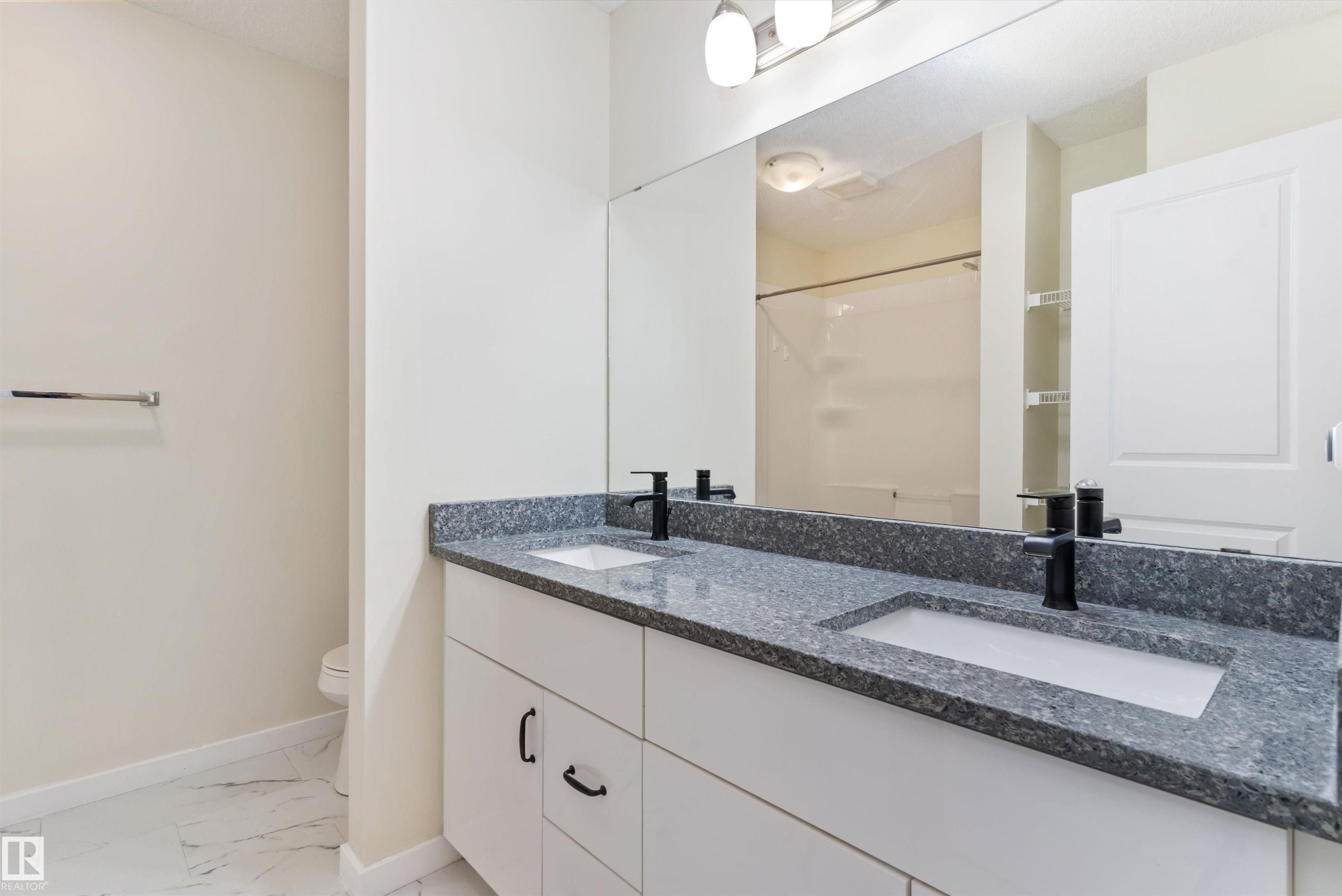 Dual vanity with granite countertop and integrated sinks, matte black fixtures, and expansive mirror - 336 Watt Boulevard, Edmonton, AB - Indoor Photo Showing Bathroom