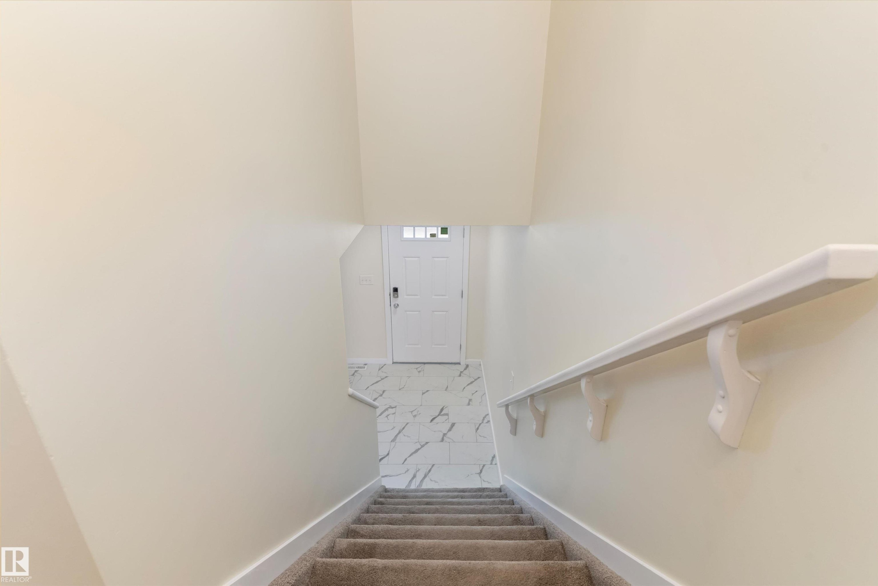 Carpeted staircase with white handrail leading to an entryway featuring large format tile flooring and a white paneled door with glass inserts - 336 Watt Boulevard, Edmonton, AB - Indoor Photo Showing Other Room