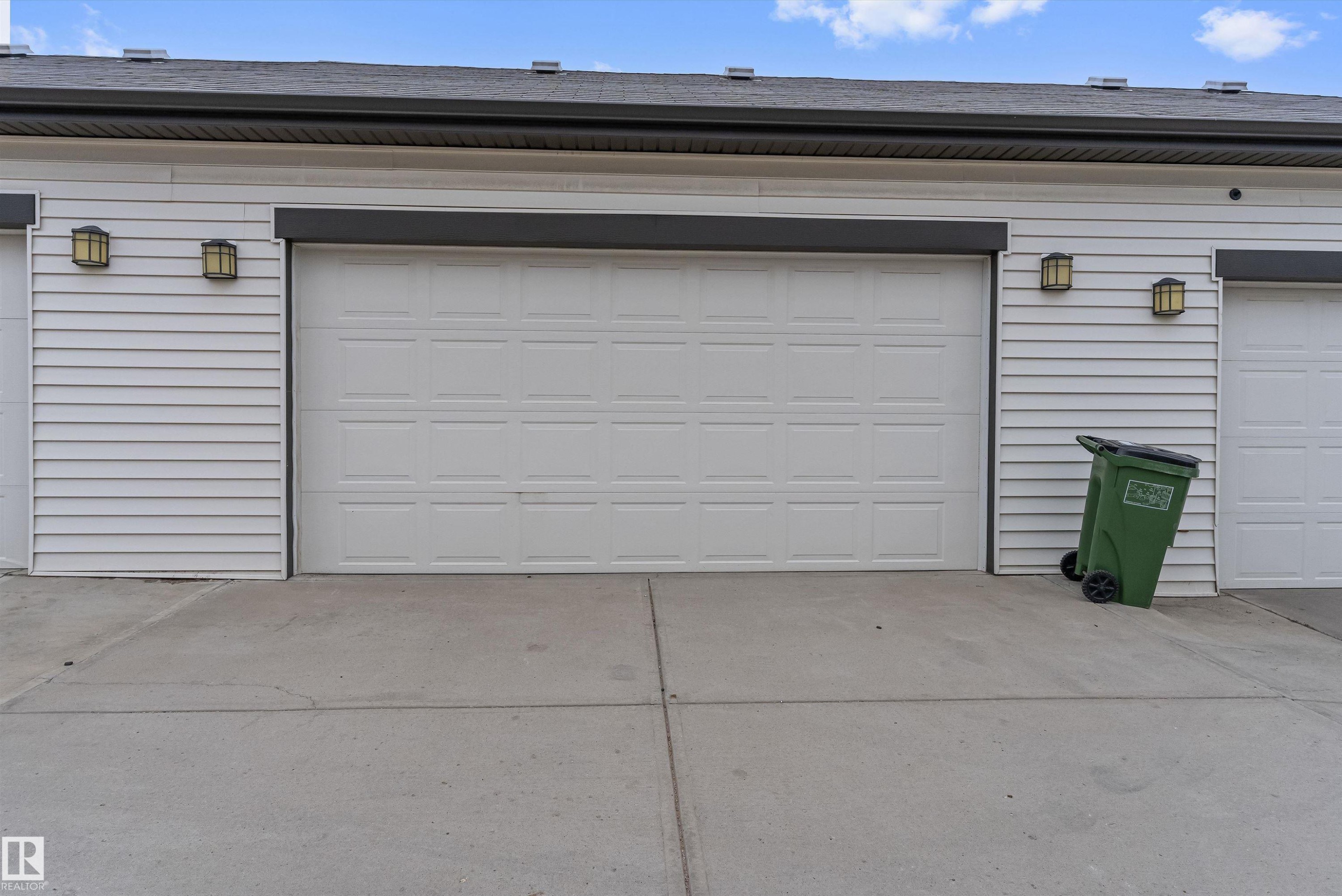 Garage exterior featuring a white paneled door, horizontal siding, dark fascia, and wall-mounted outdoor lighting fixtures - 336 Watt Boulevard, Edmonton, AB - Outdoor With Exterior