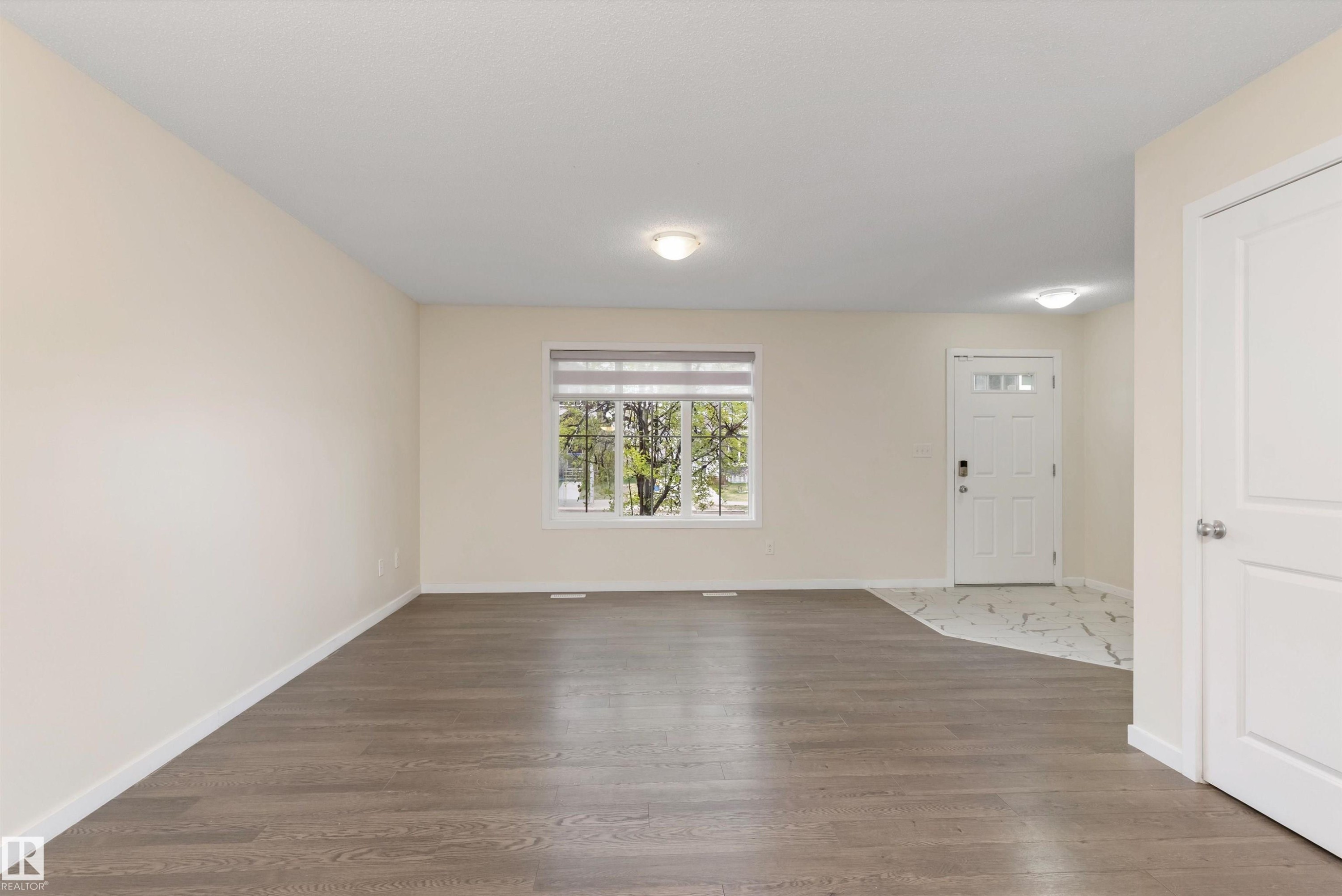 Spacious living area featuring wood-finish flooring, light neutral wall tones, and a large window with blinds - 336 Watt Boulevard, Edmonton, AB - Indoor Photo Showing Other Room