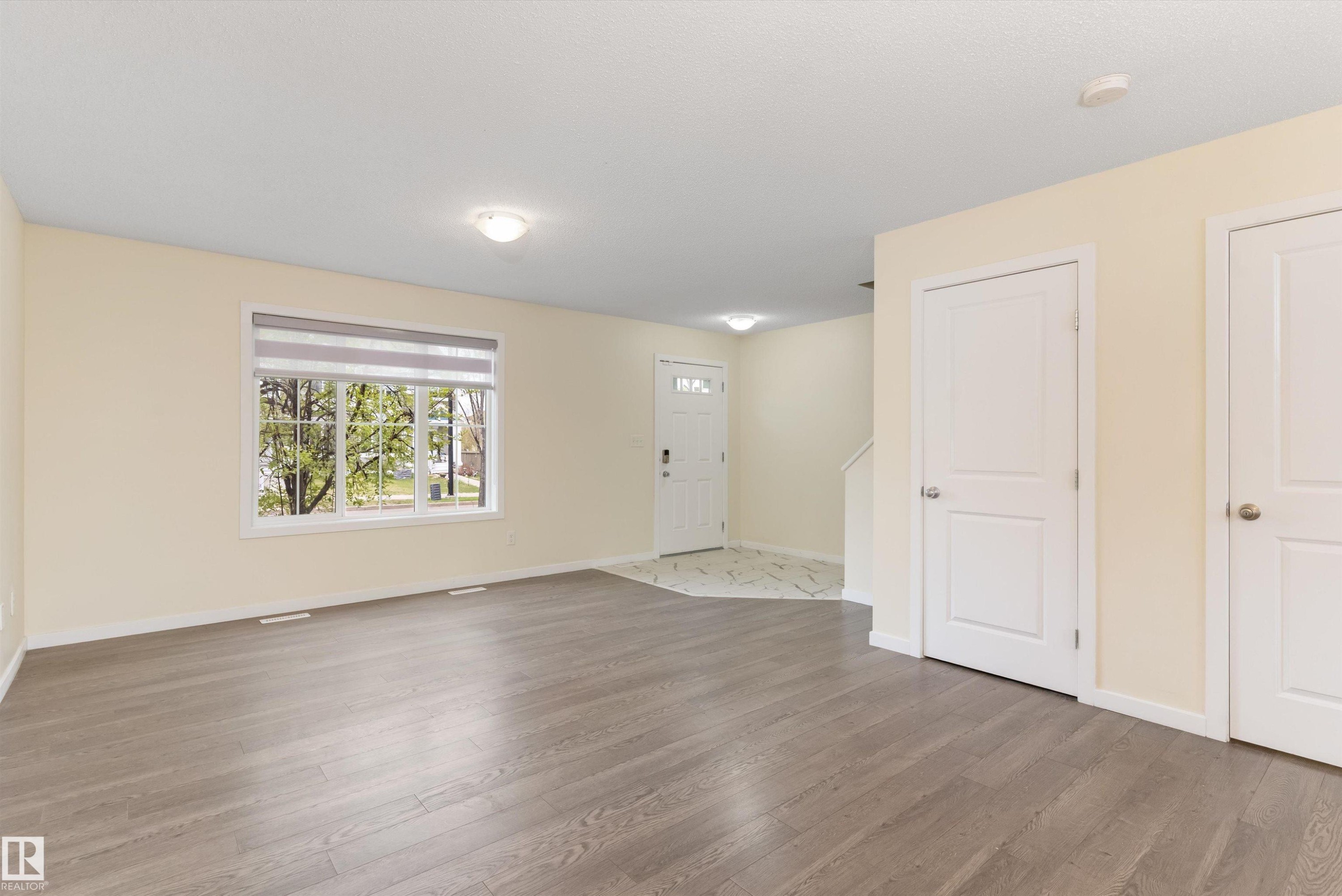 Spacious entry area featuring wood-finish flooring, a large window with roller shades, and a front entry door with decorative glass - 336 Watt Boulevard, Edmonton, AB - Indoor Photo Showing Other Room