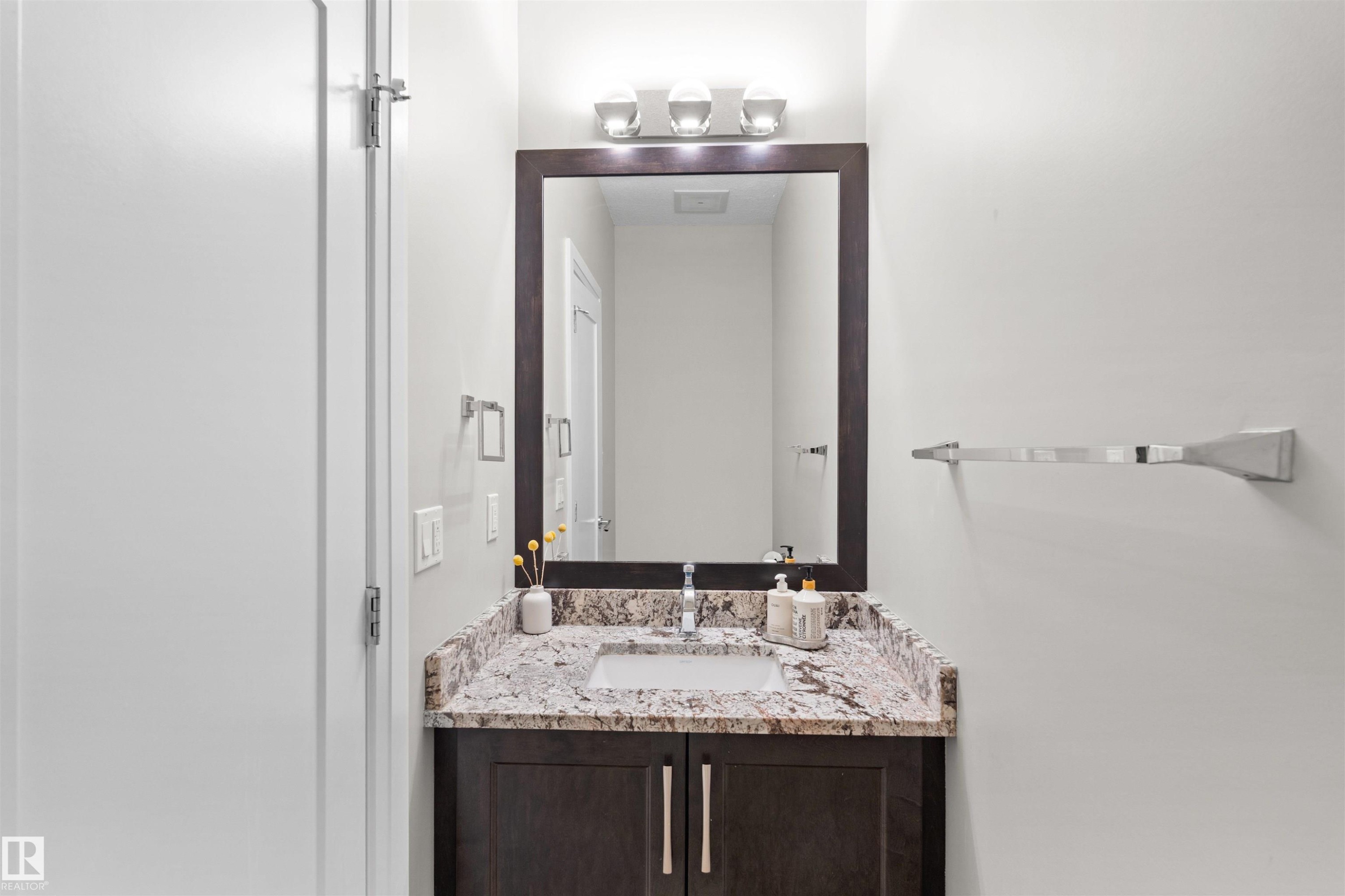 Bathroom vanity featuring a granite countertop, undermount sink, dark wood-finish cabinetry, and a framed mirror - 3807 Claxton Close, Edmonton, AB - Indoor Photo Showing Bathroom