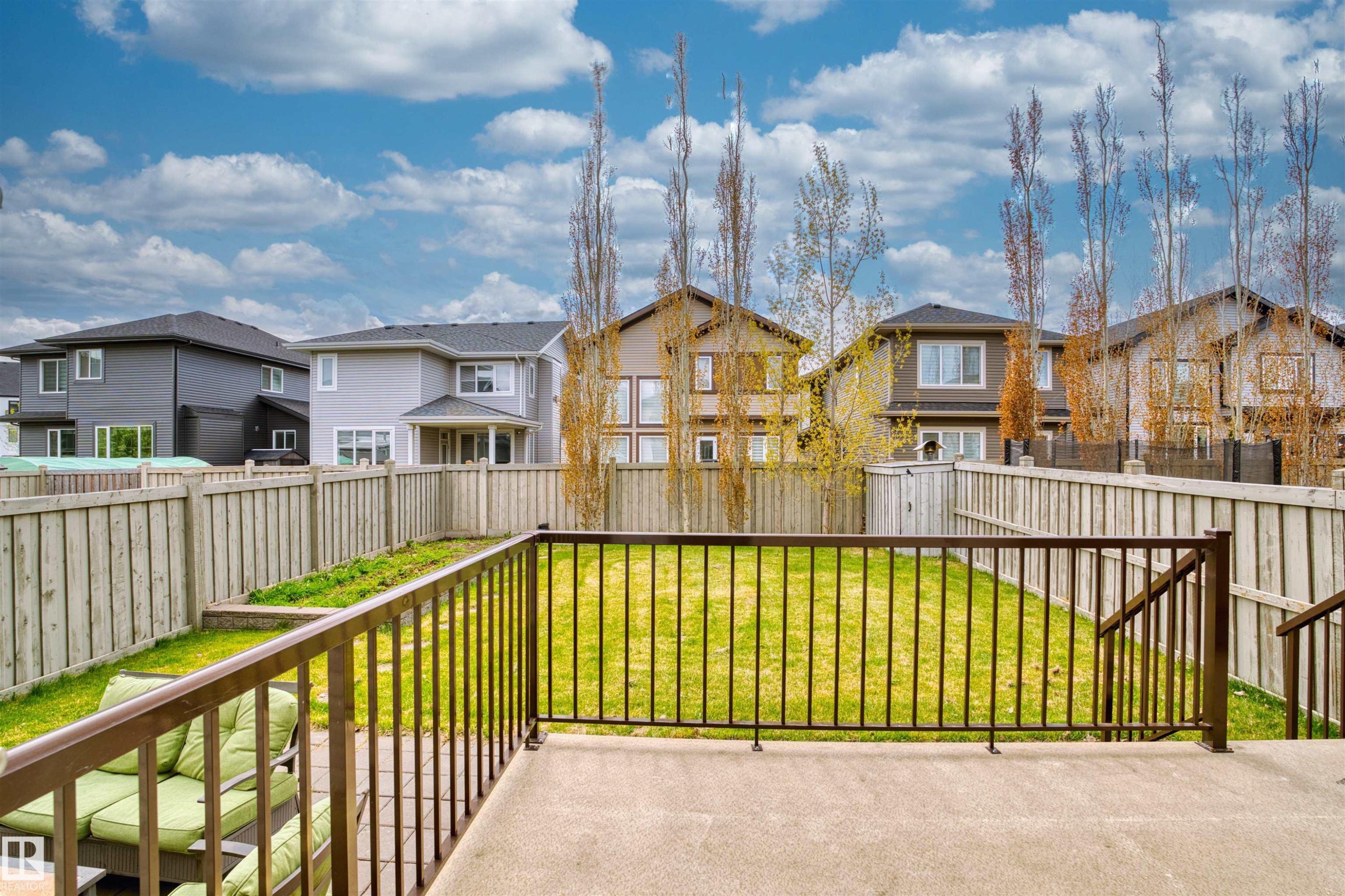 Spacious fenced backyard featuring a concrete patio, wrought iron railing, and manicured lawn - 3807 Claxton Close, Edmonton, AB - Outdoor