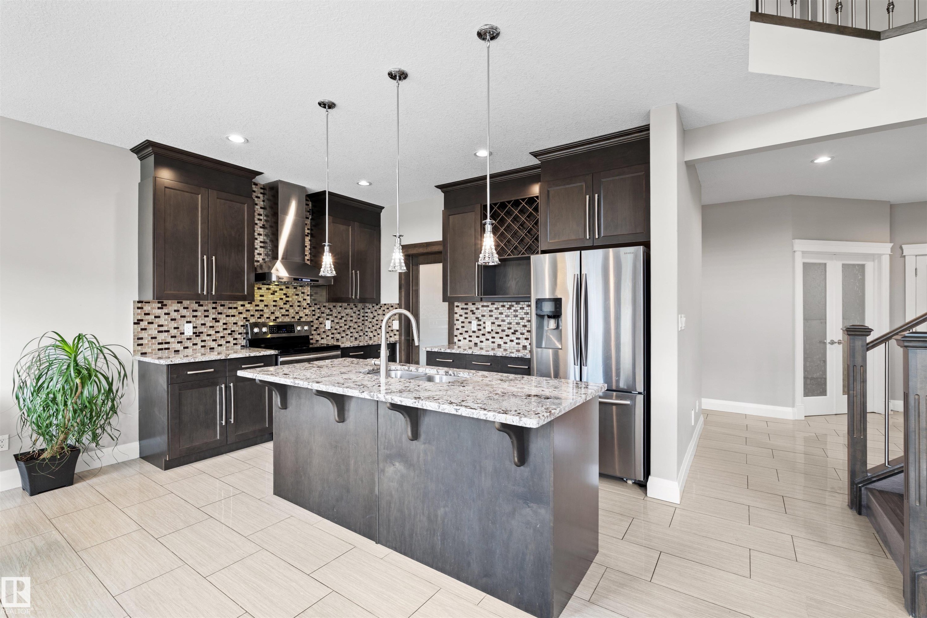 Modern kitchen featuring dark wood cabinetry, stainless steel appliances, a multi-tone tile backsplash, and a central island with a light-colored countertop - 3807 Claxton Close, Edmonton, AB - Indoor Photo Showing Kitchen With Upgraded Kitchen