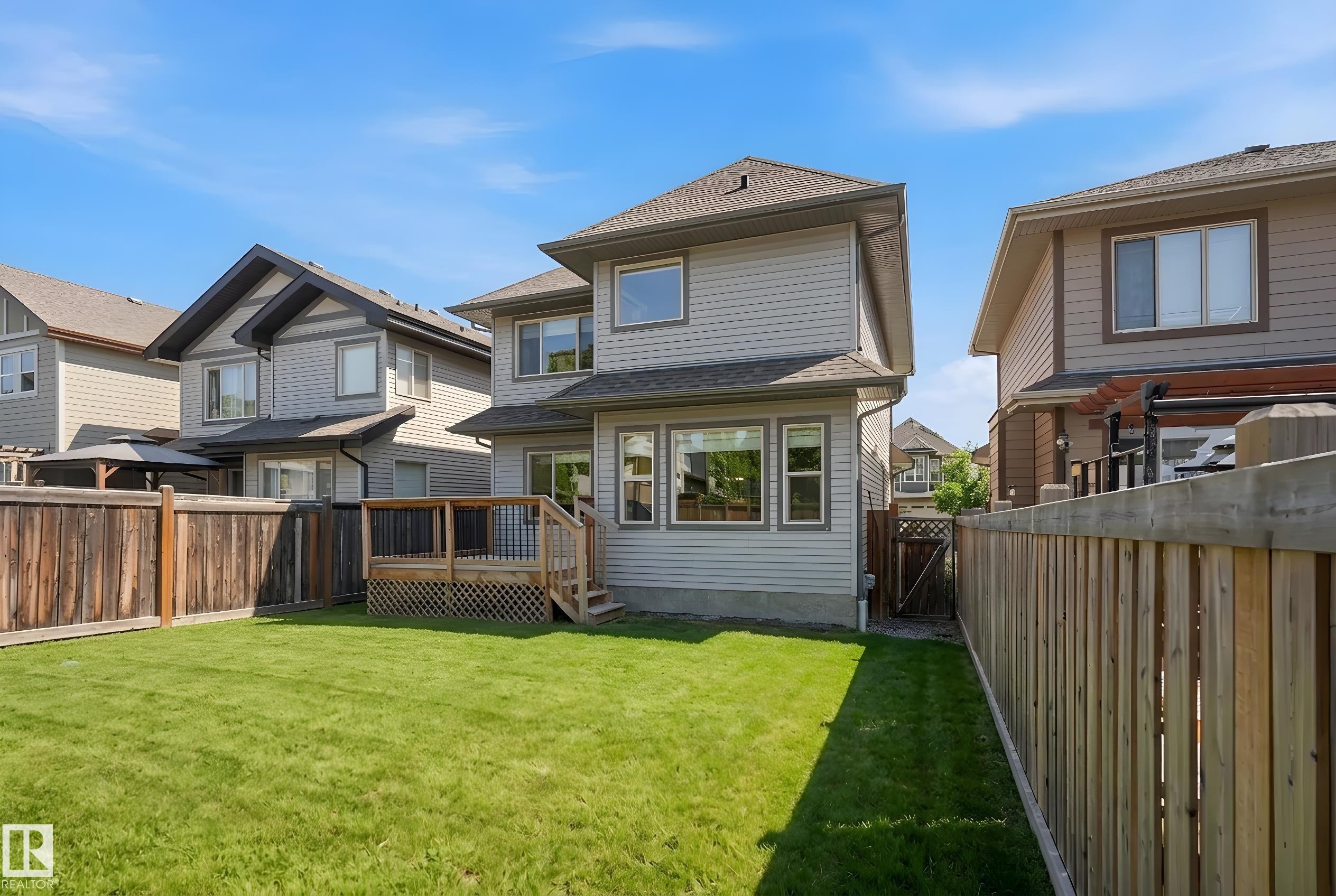 Expansive backyard featuring a manicured lawn, full wood fencing, and a raised wooden deck with lattice skirting and stairs - 469 Ainslie Crescent Sw, Edmonton, AB - Outdoor