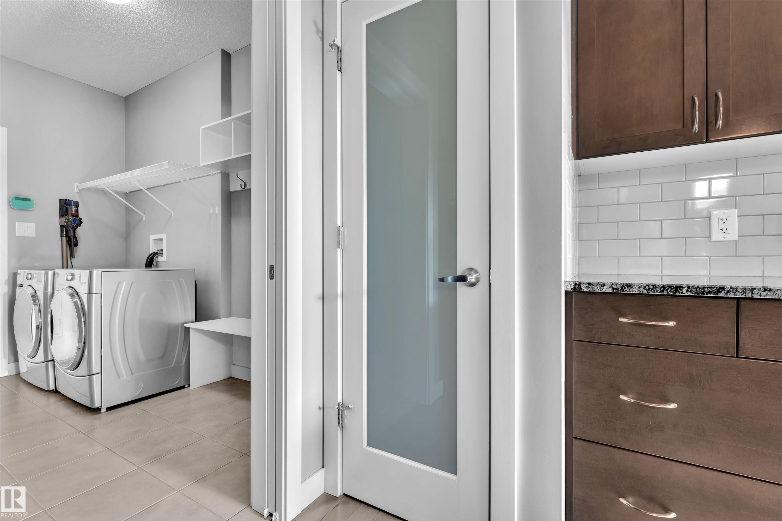 The laundry area features modern appliances, tile flooring, wall-mounted shelving, and a built-in bench - 8108 217 Street, Edmonton, AB - Indoor Photo Showing Laundry Room