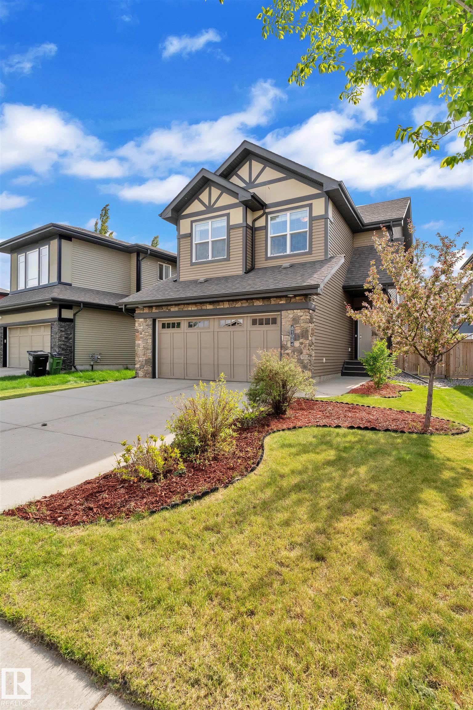 The property features a two-story exterior with a blend of siding and stone accents, a two-car garage, and a well-maintained lawn with landscaping - 8108 217 Street, Edmonton, AB - Outdoor