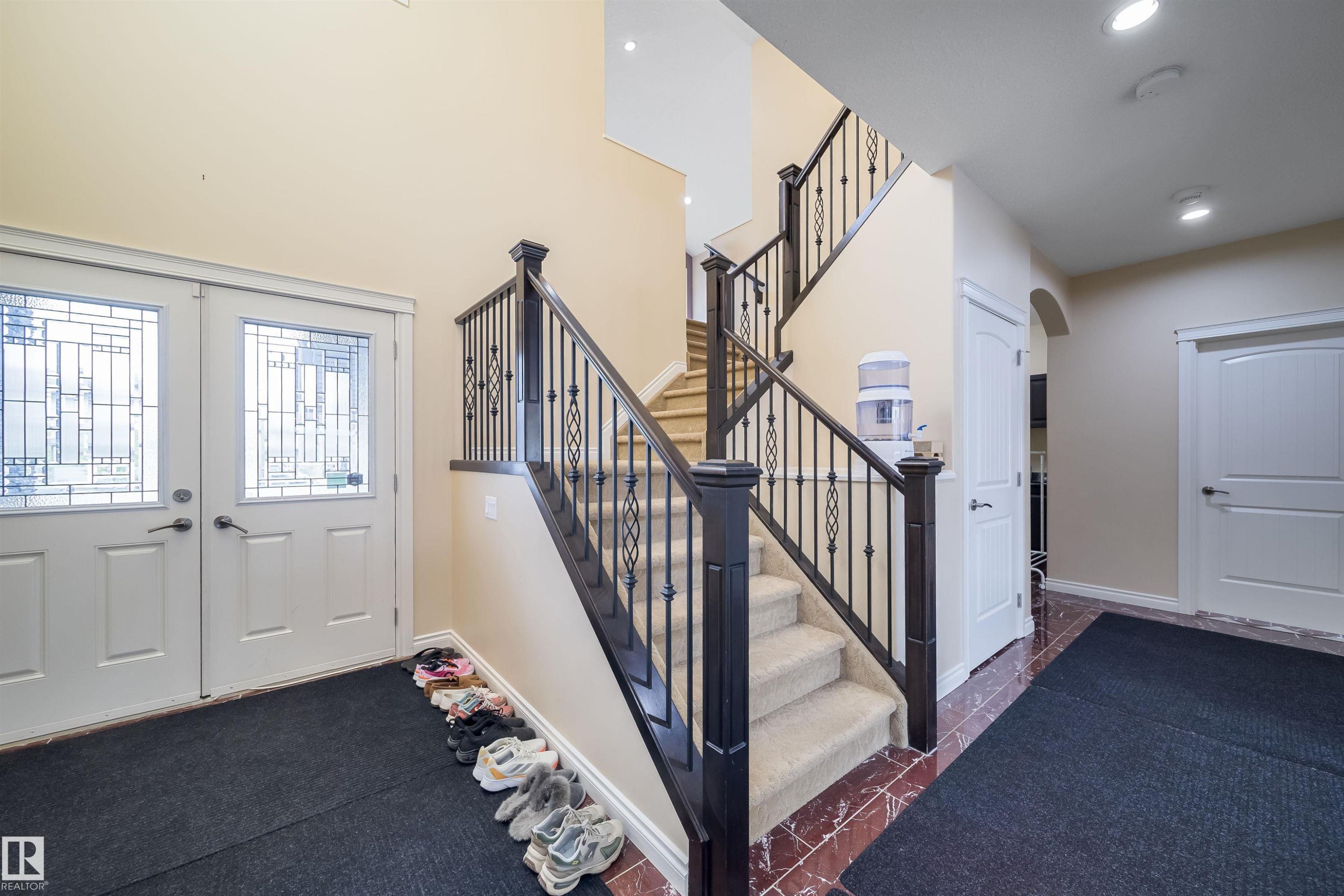 Grand foyer featuring a dual staircase with wrought iron balusters and dark wood newel posts - 1508 Cunningham Cape Cape, Edmonton, AB - Indoor Photo Showing Other Room