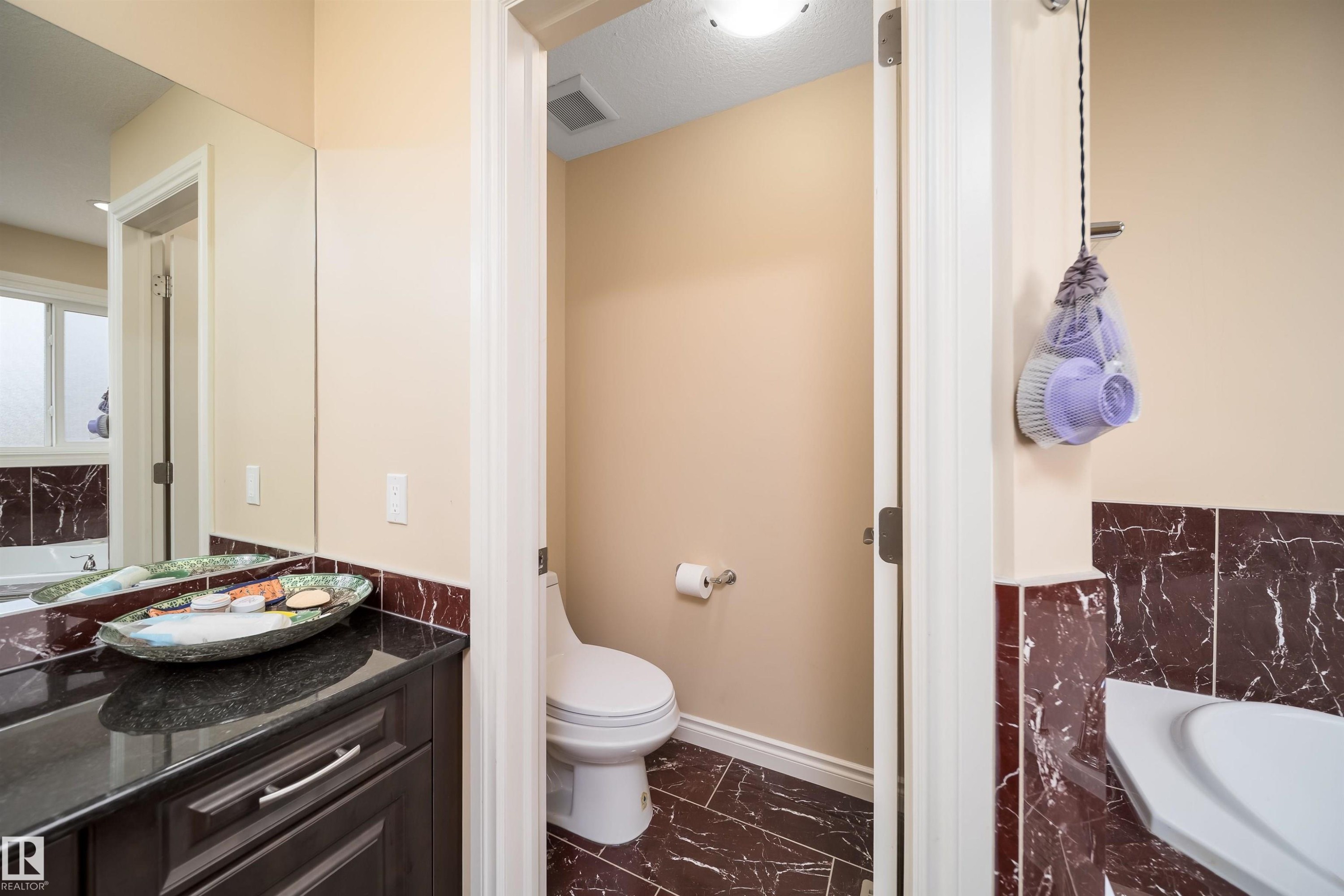 Bathroom with dark wood-finish vanity, black countertop, full-width mirror, and dark marble-look tile flooring - 1508 Cunningham Cape Cape, Edmonton, AB - Indoor Photo Showing Bathroom